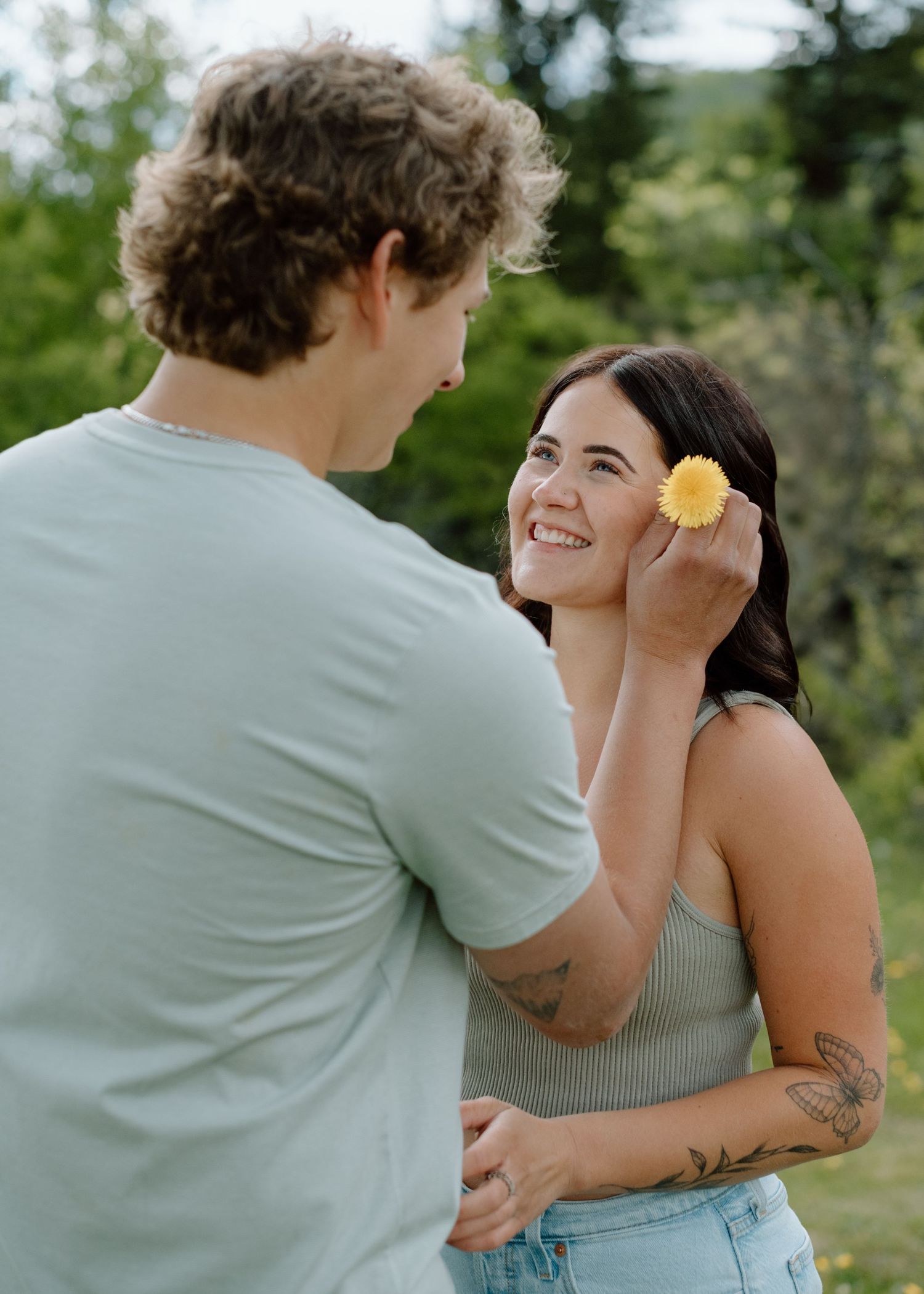 A couple playfully rolling around in a grassy meadow with mountains in the background. Calgary Alberta Engagement Photographer.