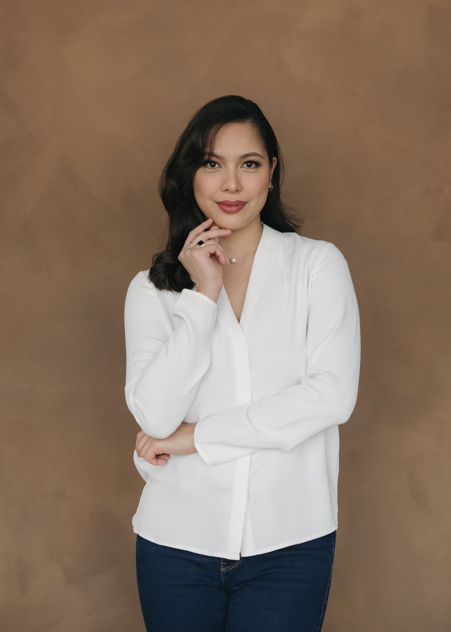 A person in a white button-down shirt and dark pants poses against a brown backdrop in a professional photo series.
