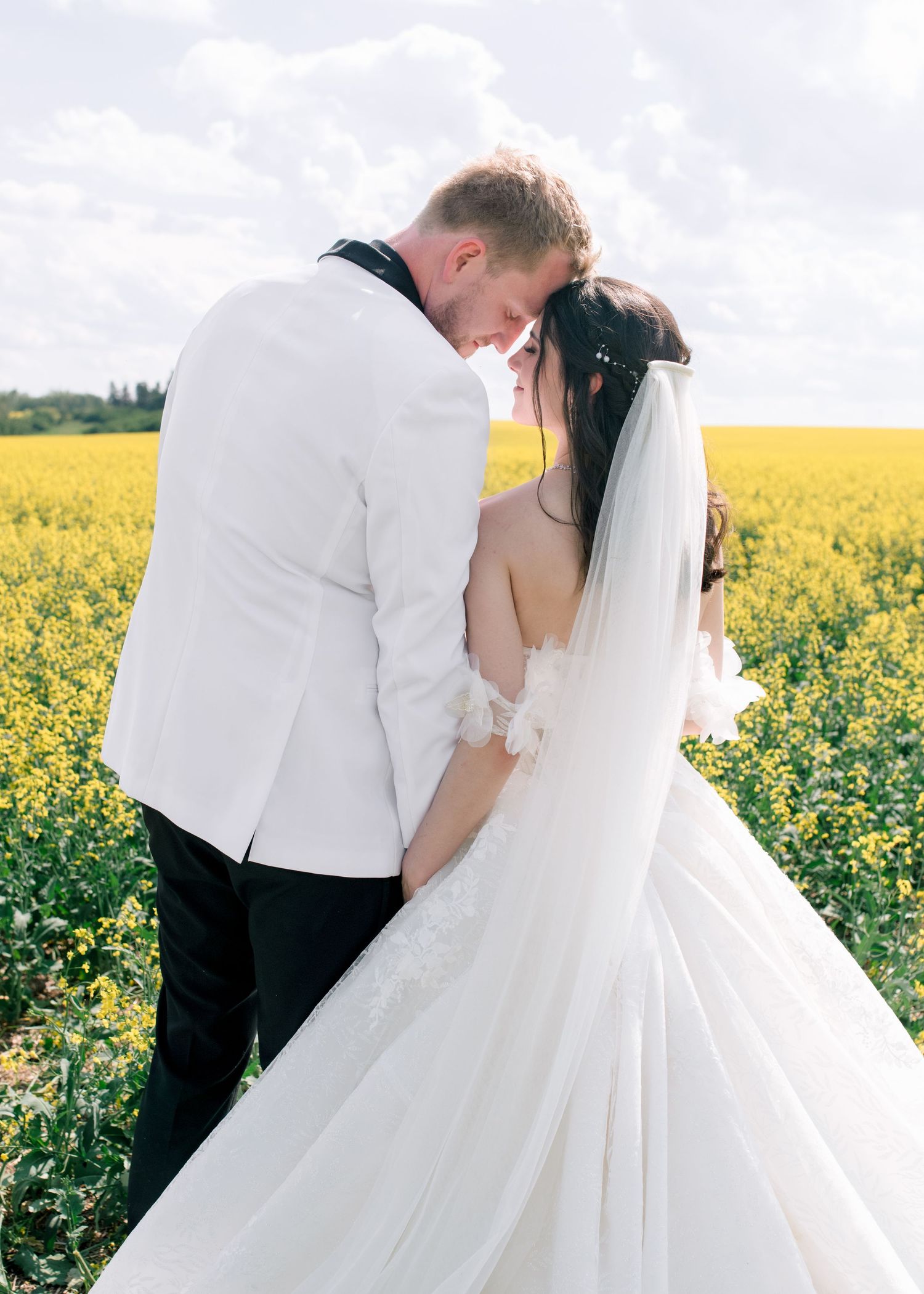 Wedding couple shares romantic moment in blooming yellow canola field during springtime outdoor photoshoot.