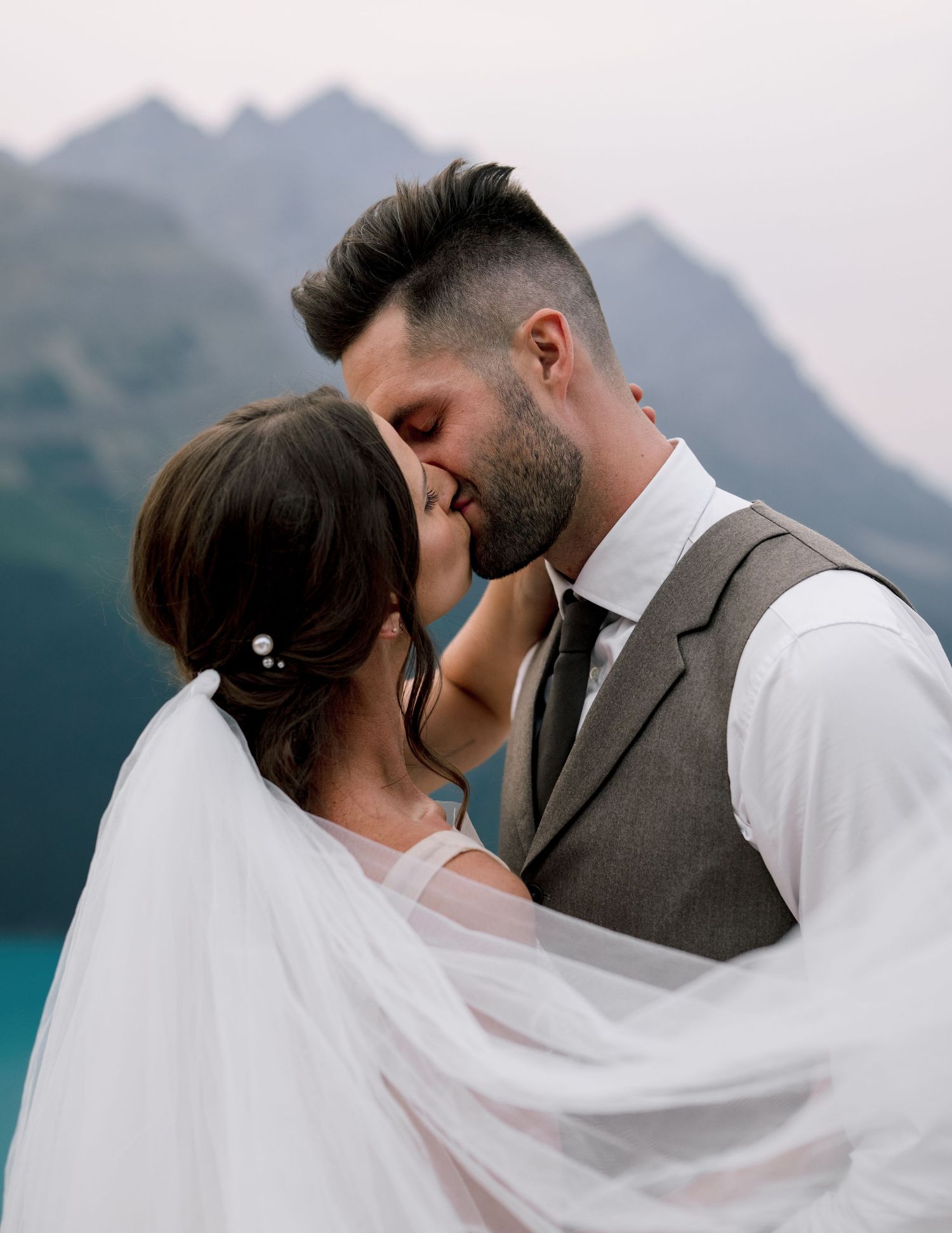 A romantic couple embraces with a flowing veil against a backdrop of majestic mountain peaks.