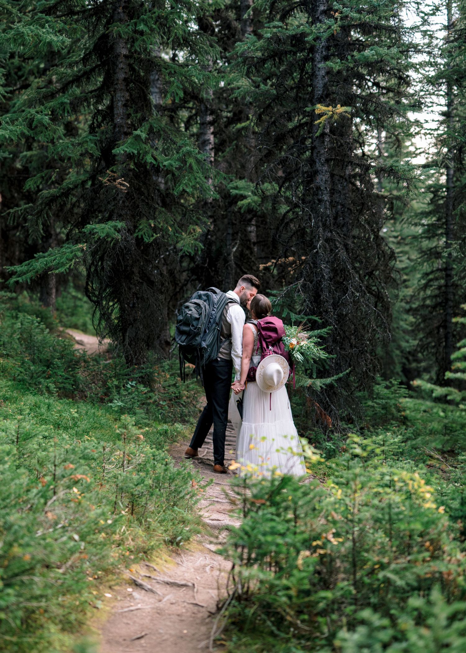 Couple walking down a scenic forest trail surrounded by evergreen trees and lush foliage during a hike.