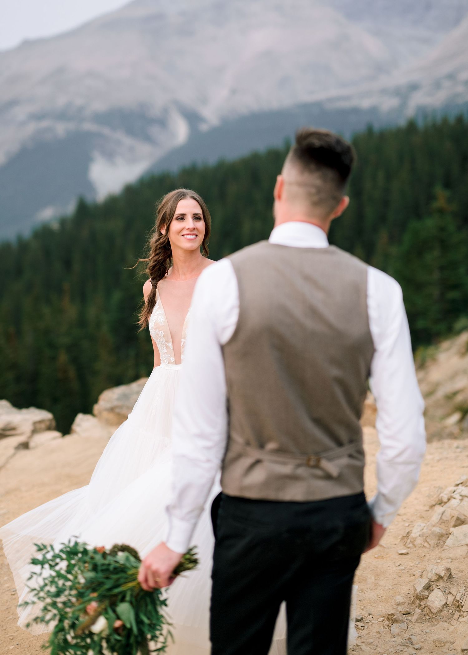 The newlyweds share a romantic moment on a mountain trail with majestic snow-capped peaks in the background.