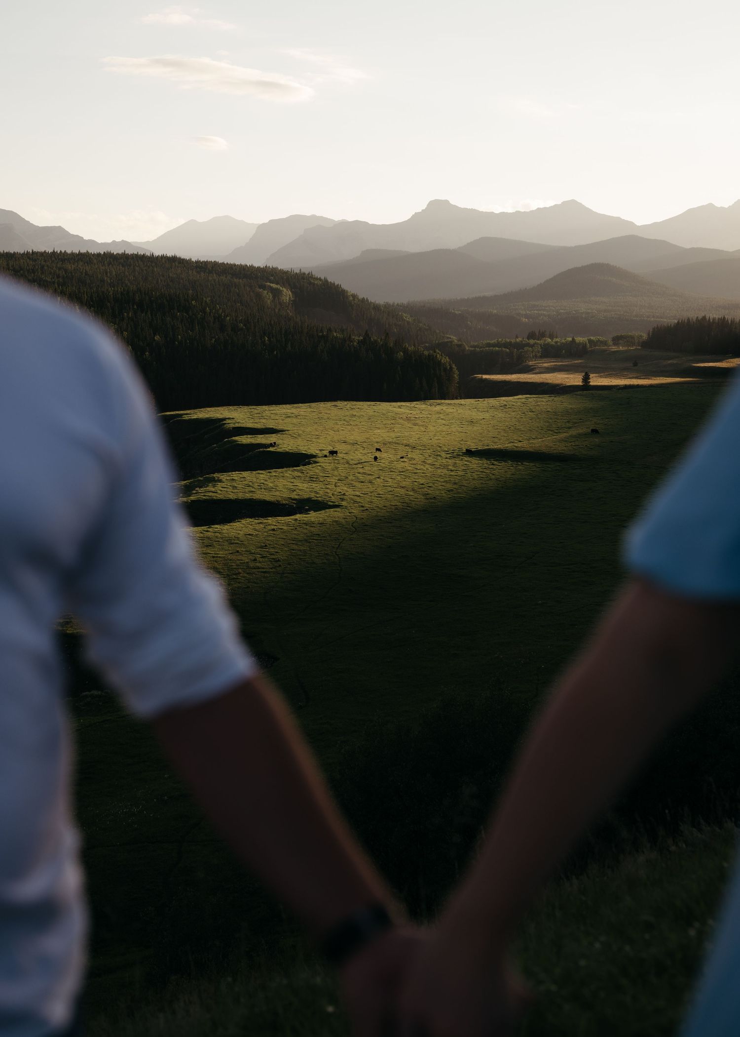 Silhouetted figures walk hand in hand along a mountain ridge at sunset with dramatic landscapes in the background.
