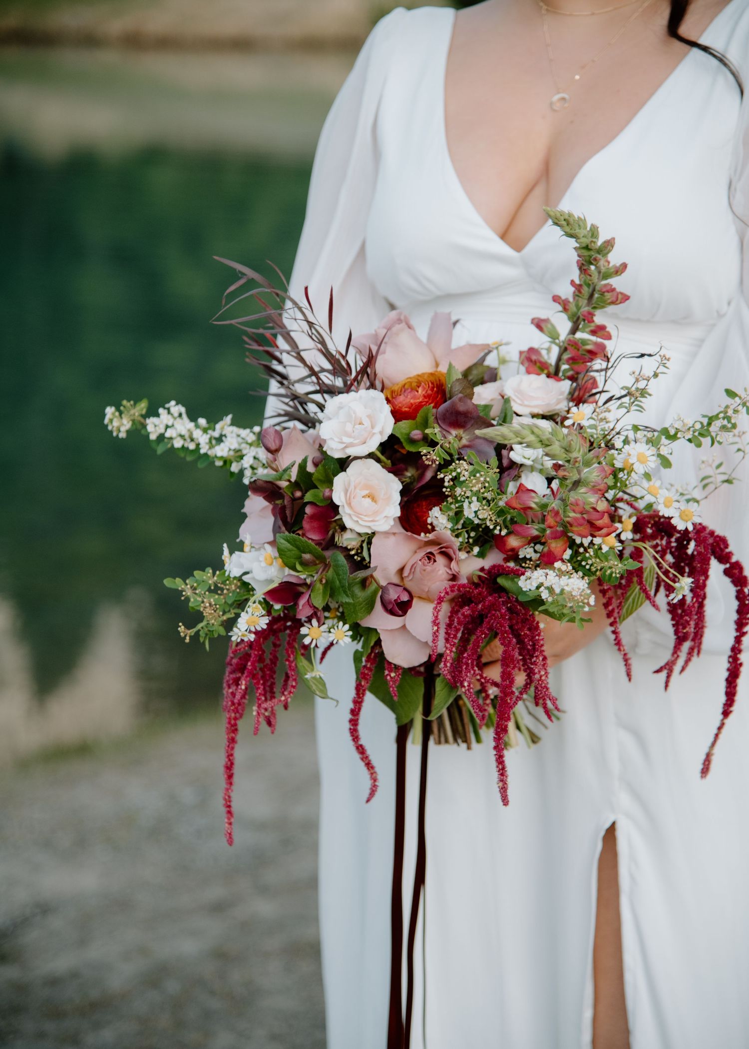 A stunning bridal bouquet with burgundy amaranthus, roses, and mixed florals against a white wedding dress. Banff and Calgary Wedding