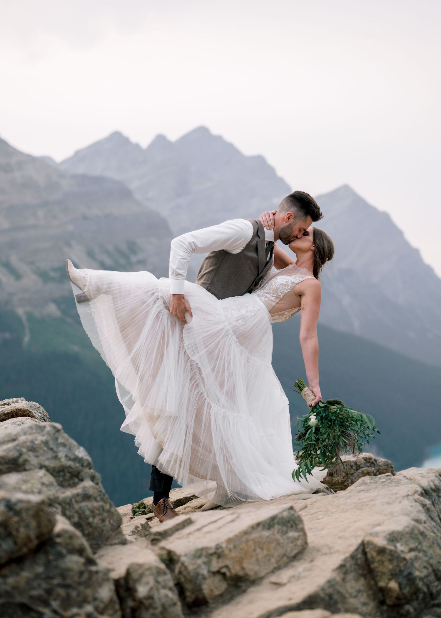 A couple shares romantic dips against the backdrop of majestic mountain peaks in a series of wedding photos.