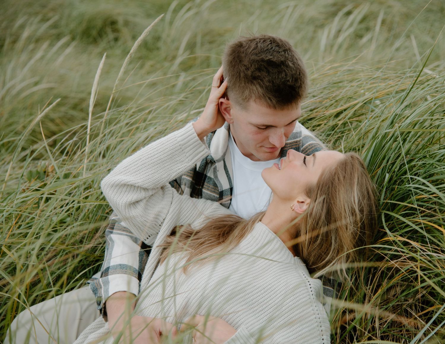 Intimate couple poses in tall beach grass during romantic photoshoot on Oregon Coast. Calgary Lifestyle and Engagement Photographer.