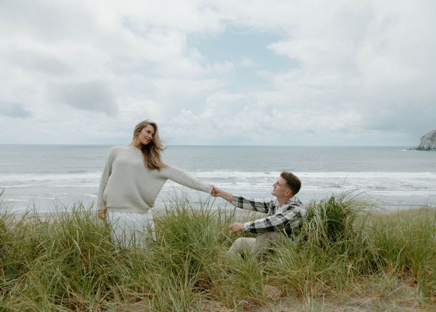 Romantic beachside scene with tall grass and cloudy coastal skies.