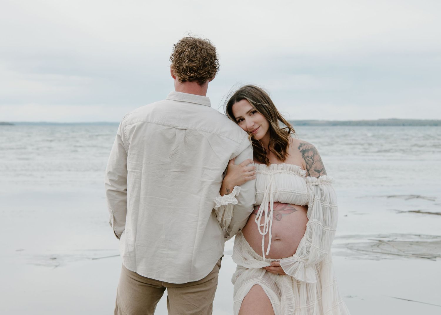 Intimate maternity beach portrait with couple in light coloured clothing against ocean backdrop. Calgary Alberta Maternity Photographer.