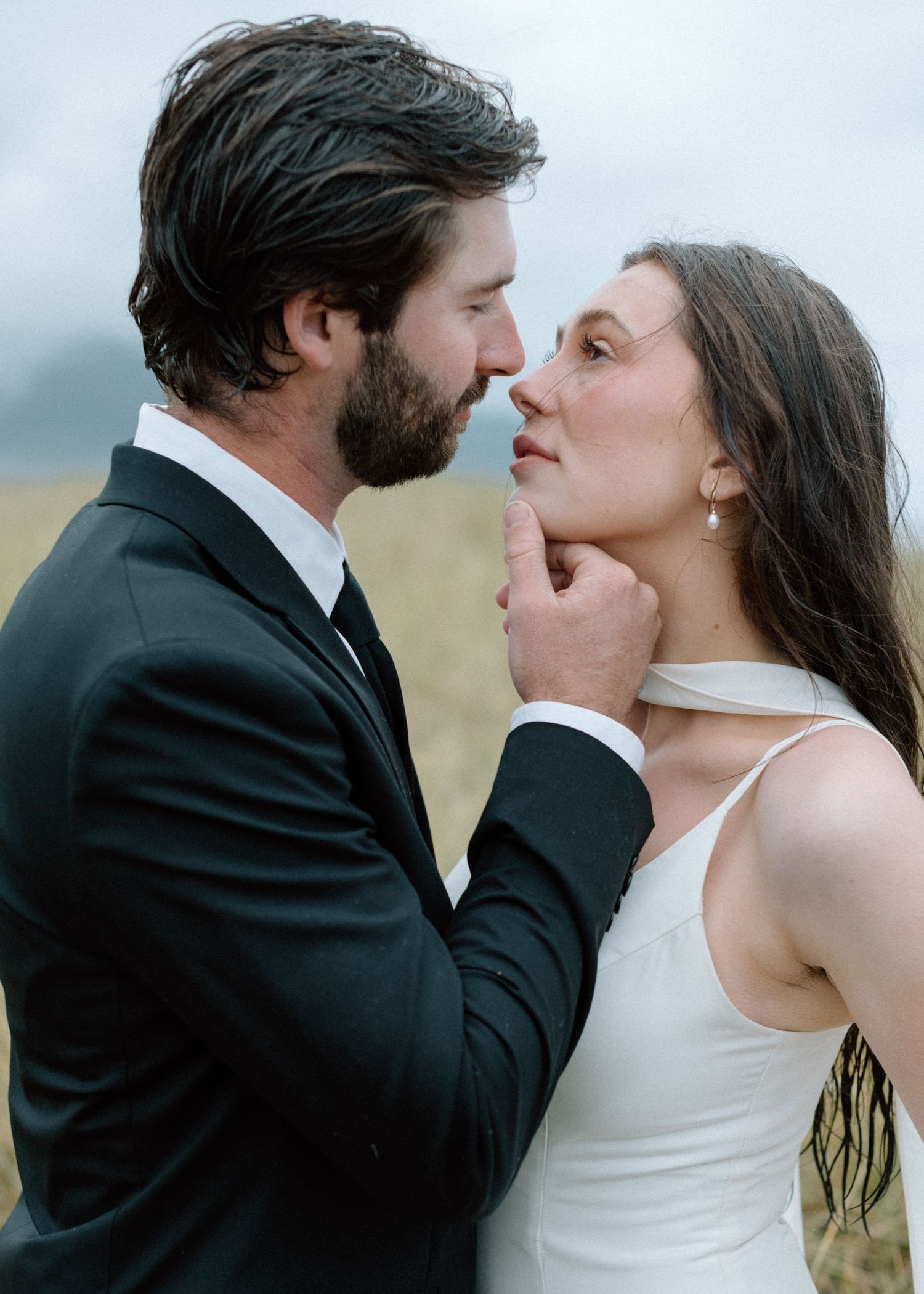 Intimate moment between a couple in formal wedding attire standing close together in an outdoor setting at dusk.