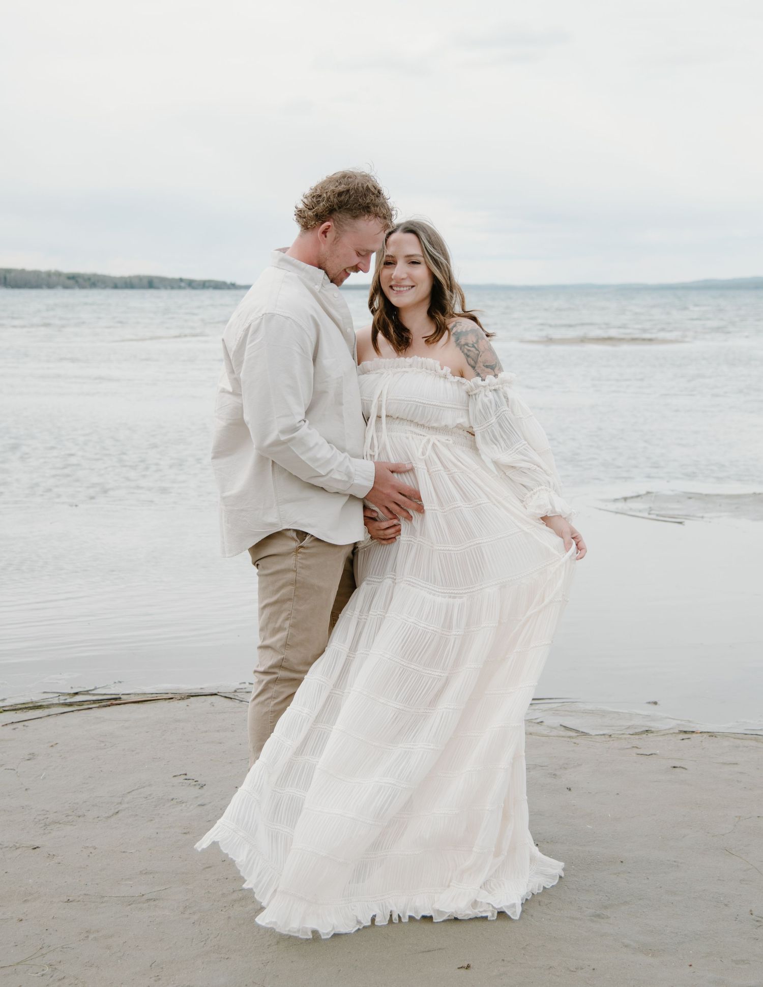 A dreamy maternity photo with a couple in light colors against a beach backdrop. Calgary Alberta Maternity Photographer.