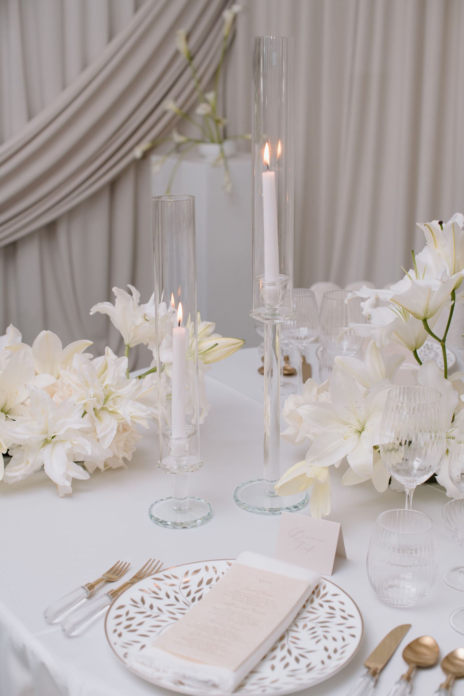 White table setting with tall glass candleholders, white lilies, and delicate place settings at the Brownstone YYC. Calgary Wedding Photo