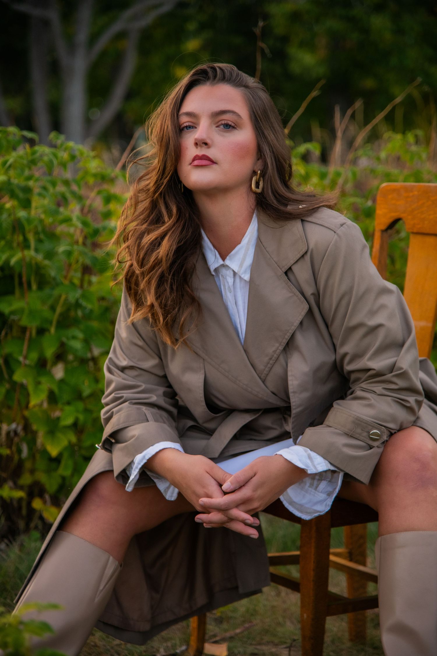 Outdoor portrait in beige trench coat and boots against garden backdrop. Calgary Alberta Branding Photographer.