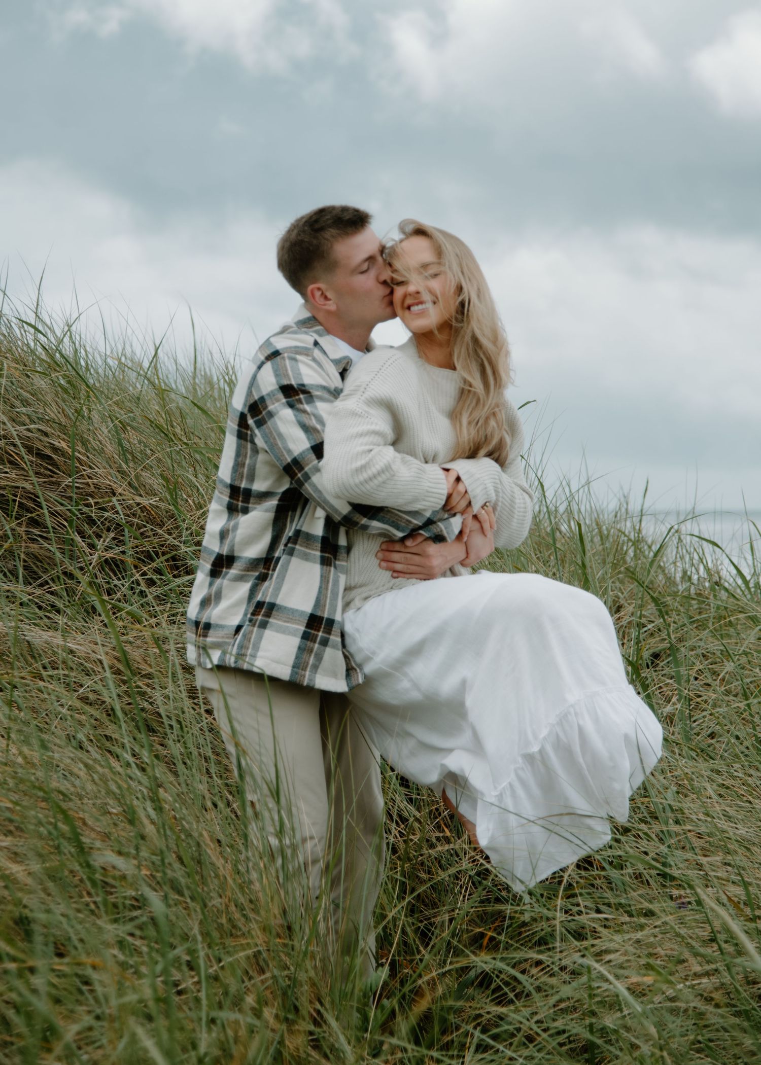 A romantic kiss shared between a couple on a grassy coastal hillside on Oregon Coast. Calgary Lifestyle and Engagement Photographer.