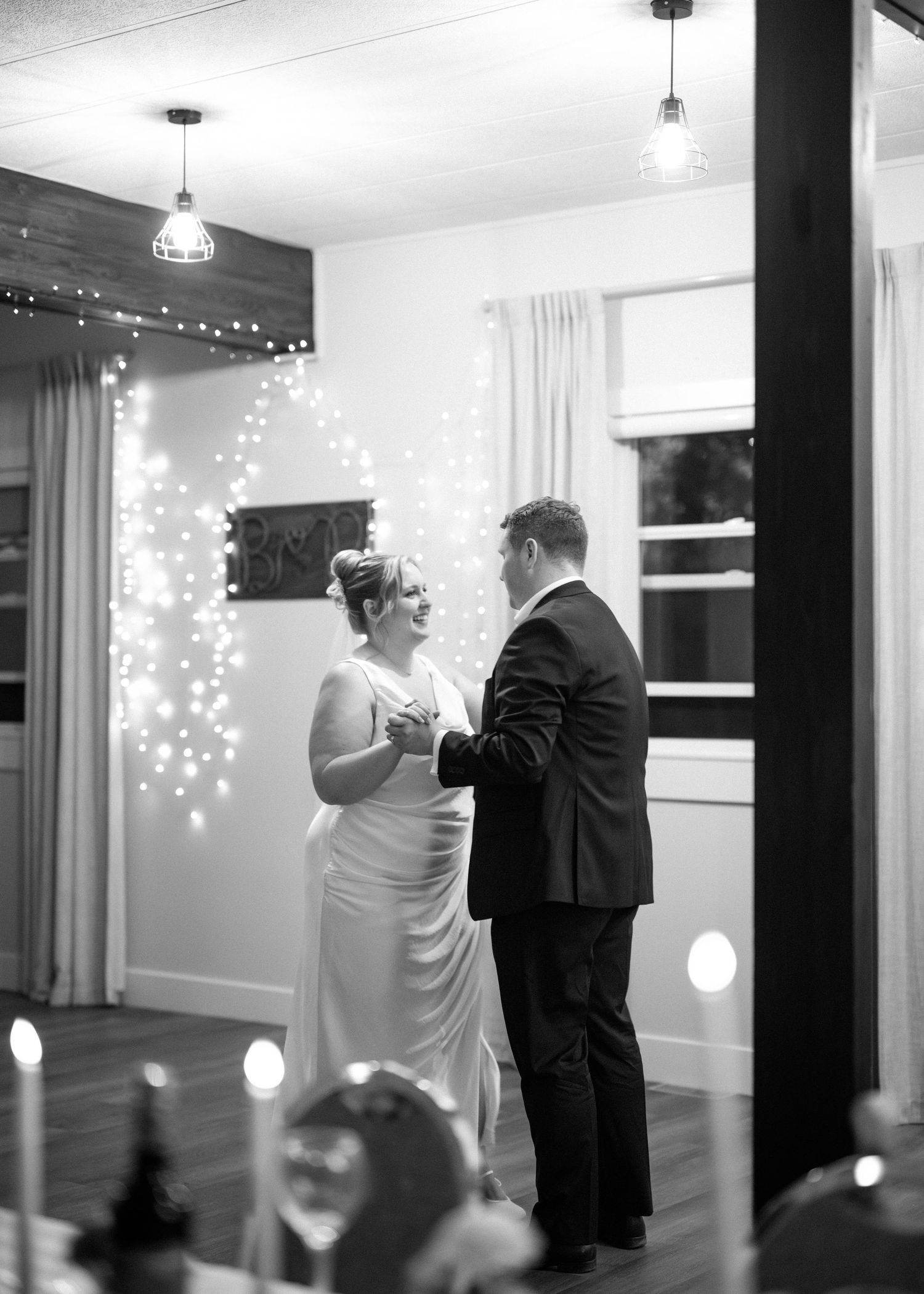 A couple shares a romantic first dance at their wedding reception with twinkling lights illuminating the background.
