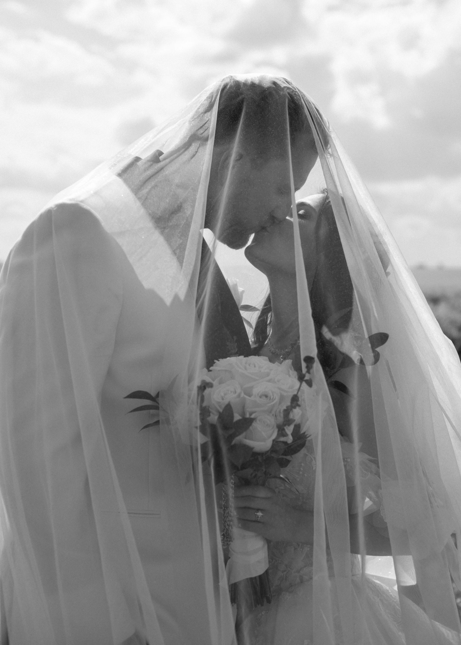 Row of ghostly figures draped in white veils stand in line against a cloudy sky background.