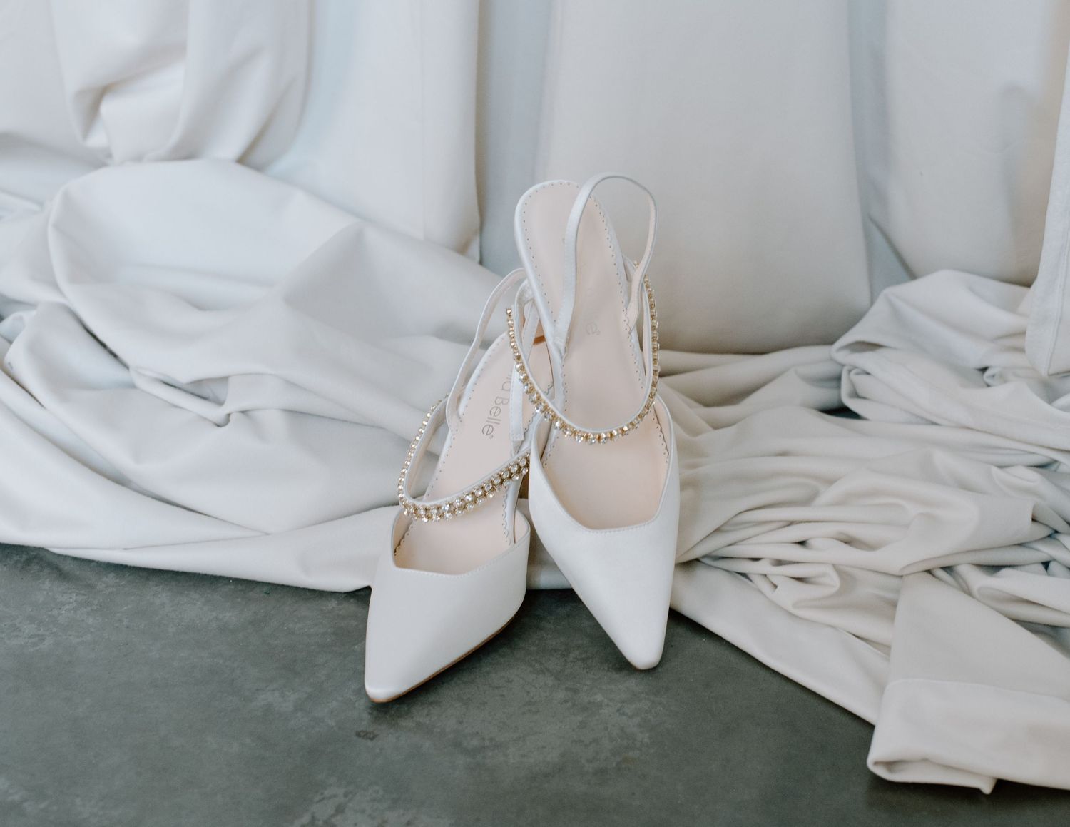 Elegant white bridal shoes and dress details arranged on light background at the Brownstone YYC. Calgary Wedding Photographer