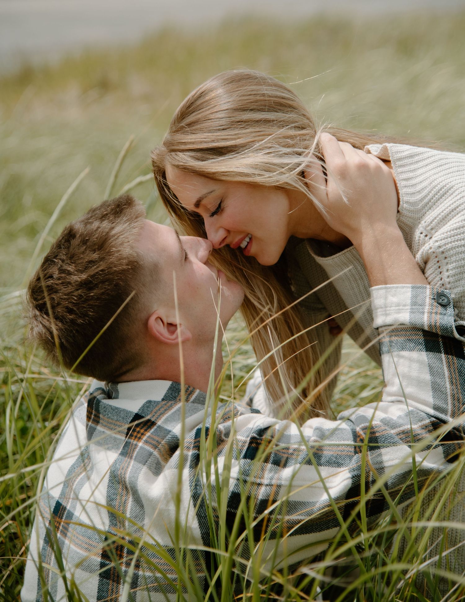 Couple laying in windswept beach grass during an overcast day by the ocean on Oregon Coast. Calgary Lifestyle and Engagement Photographer.
