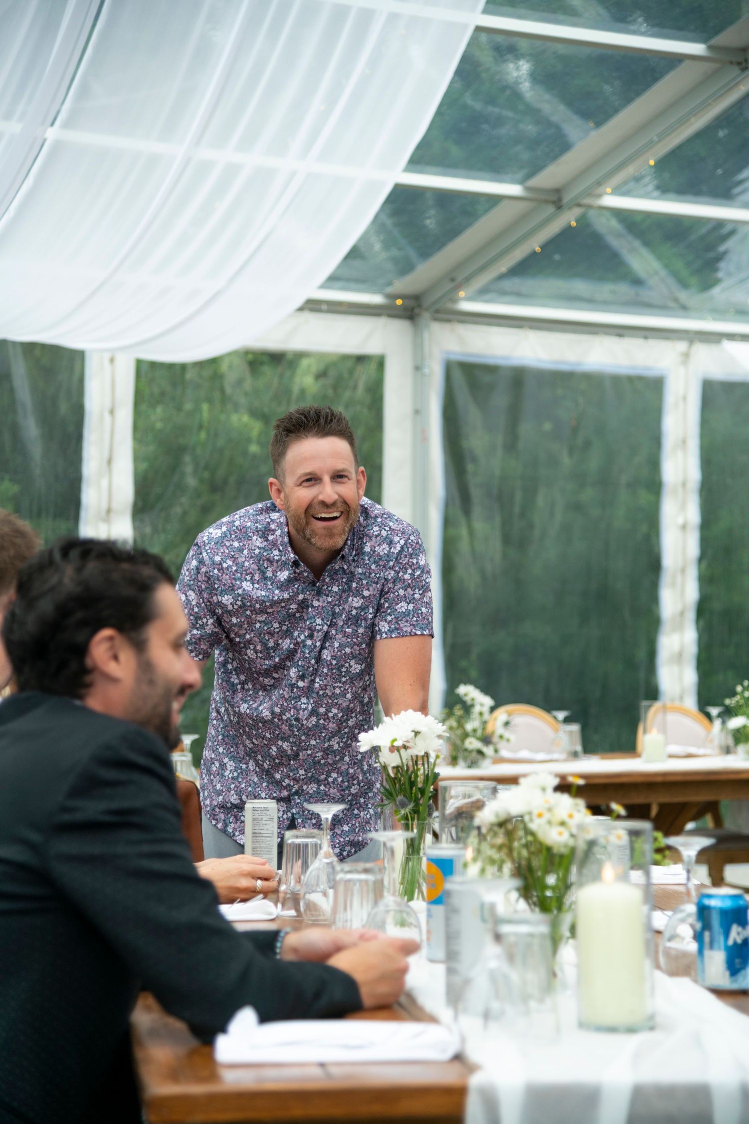 Wedding reception guest sharing laughs at table under clear tent pavilion. Calgary Wedding Photographer