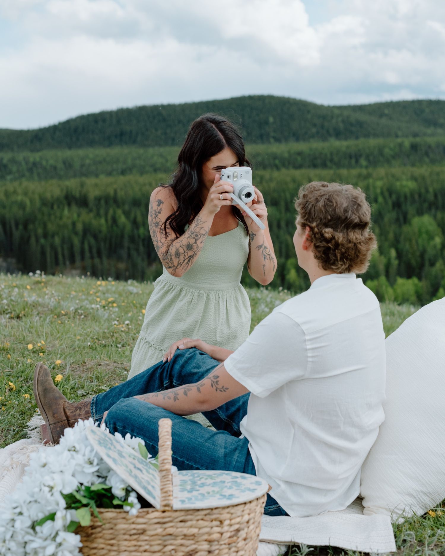 A couple enjoys a picnic on a blanket surrounded by mountain scenery and wildflowers. Calgary Alberta Engagement Photographer.