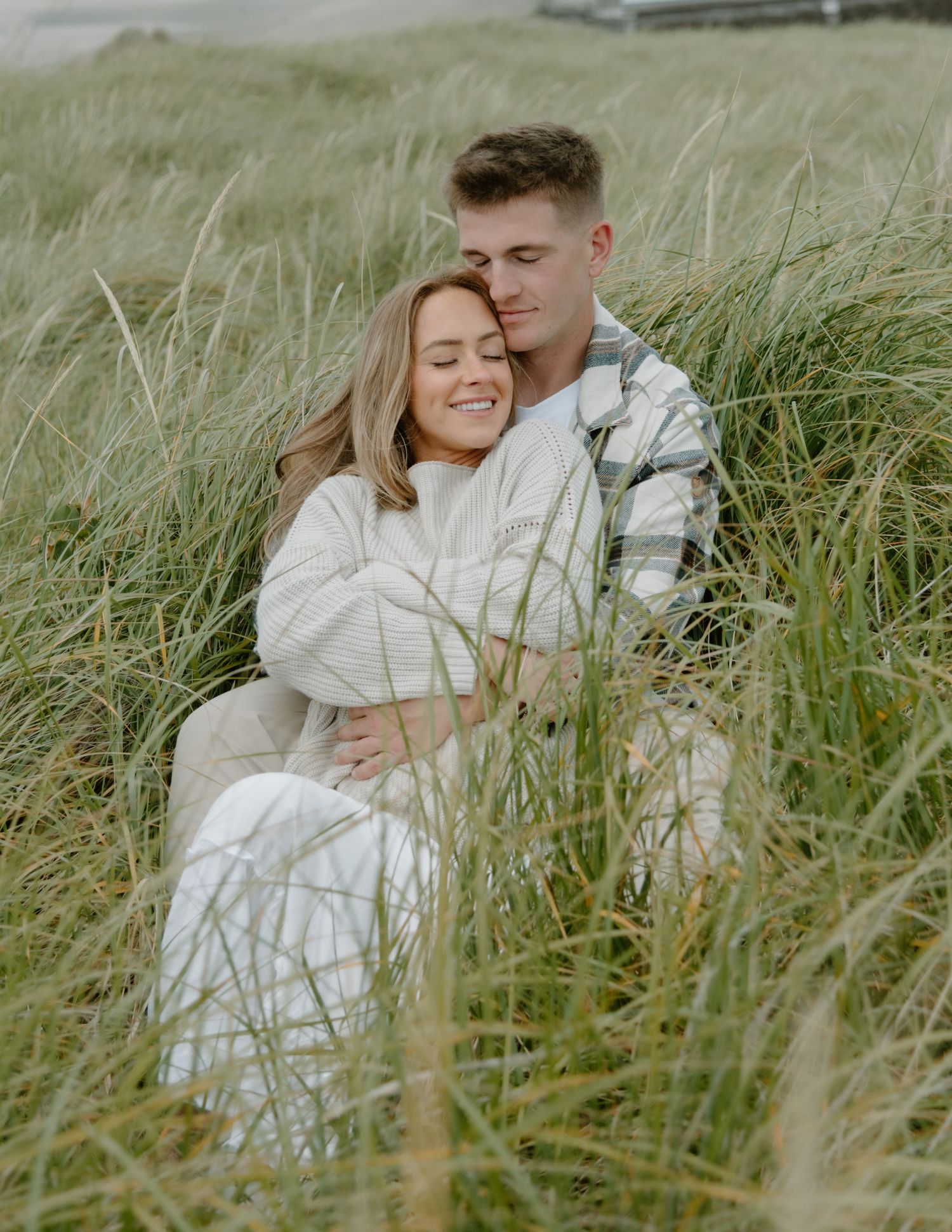 Tender moment captured between couple in natural beach grass setting on Oregon Coast. Calgary Lifestyle and Engagement Photographer.