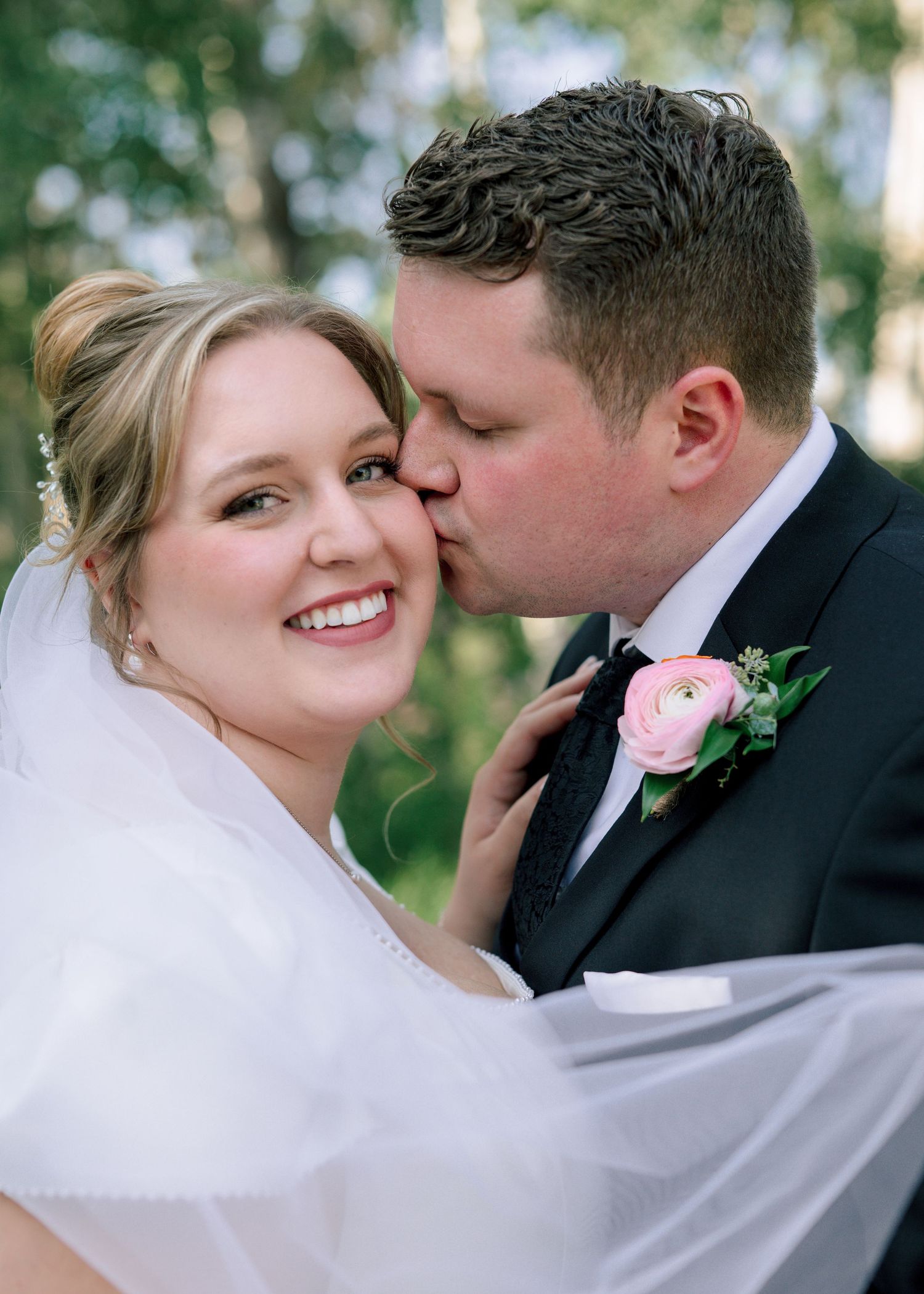 A couple shares intimate moments on their wedding day with the bride wearing a flowing white veil in an outdoor setting.
