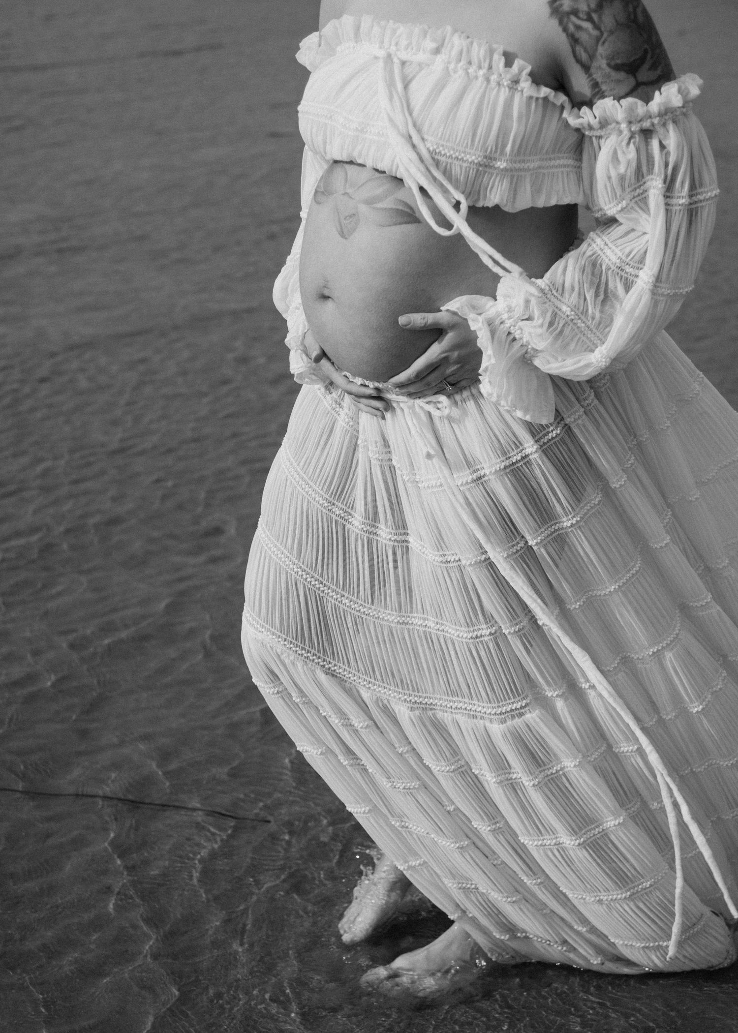 Black and white detail shot of maternity dress with textured fabric near water. Calgary Alberta Maternity Photographer.