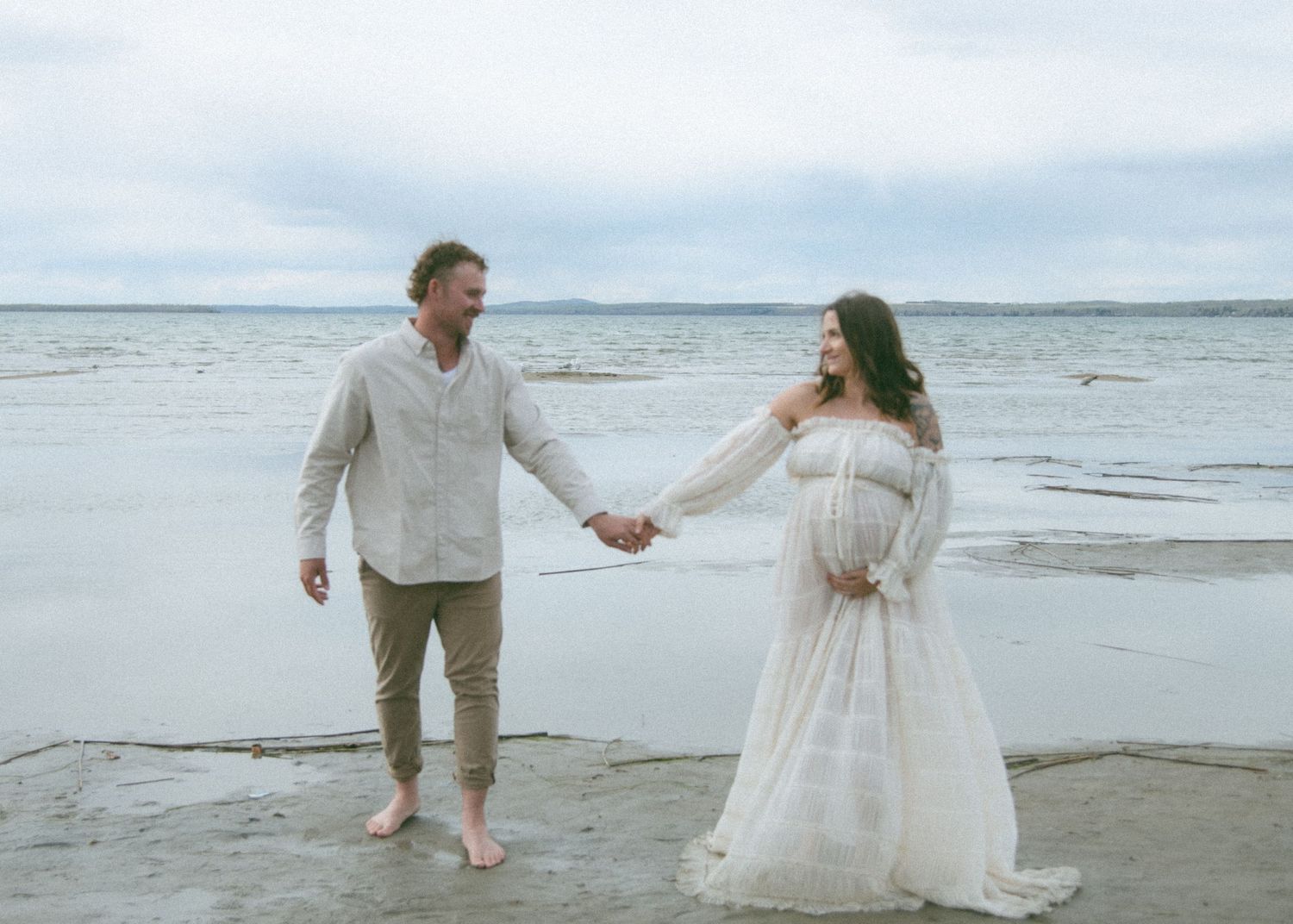 A romantic beach scene with two people walking and holding hands by the ocean. Calgary Alberta Maternity Photographer.