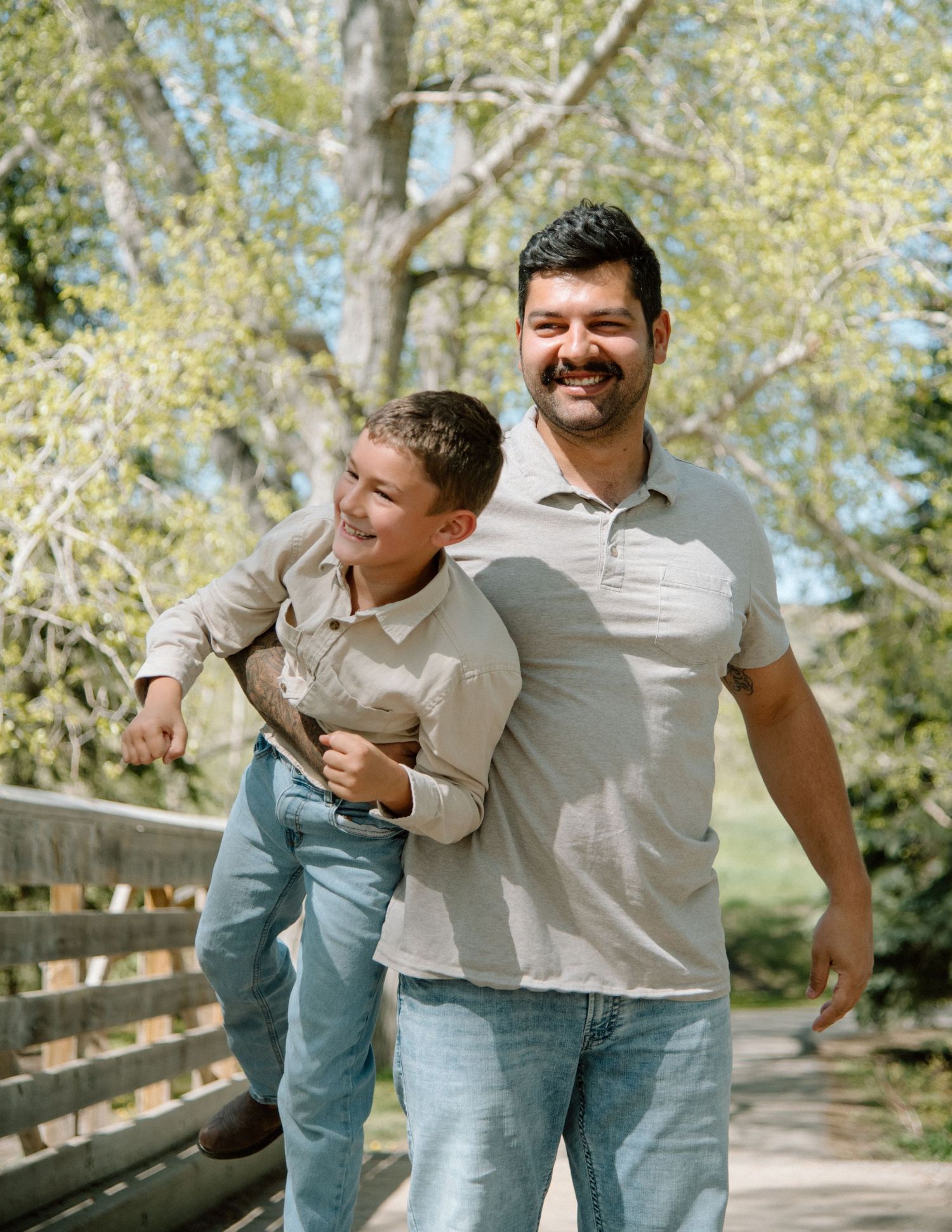 A playful moment captured outdoors on a wooden walkway surrounded by trees on a sunny day. Calgary Alberta Family Photographer.