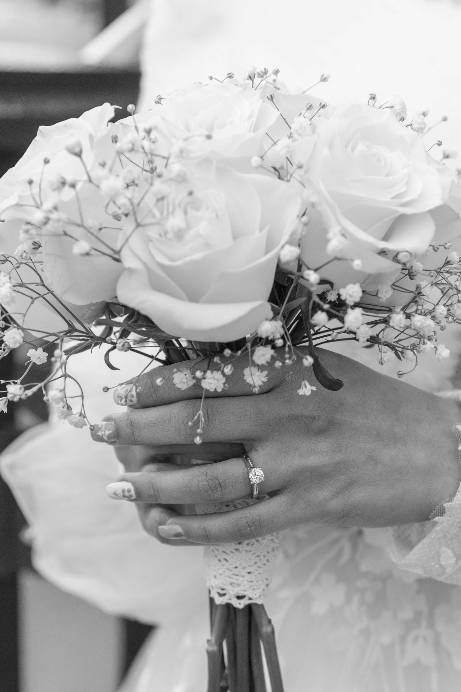 Black and white photo of hands holding a white rose and baby's breath wedding bouquet. Calgary Wedding Photographer
