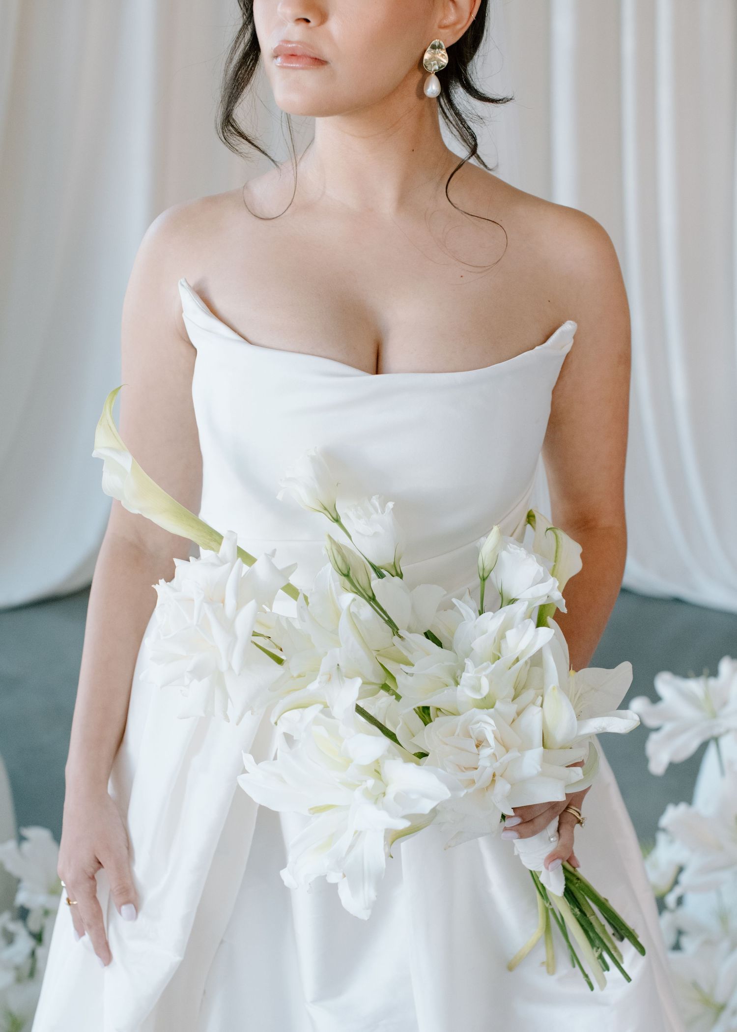An elegant bride holds a bouquet of white lilies while wearing a strapless wedding dress at the Brownstone YYC. Calgary Wedding Photographer