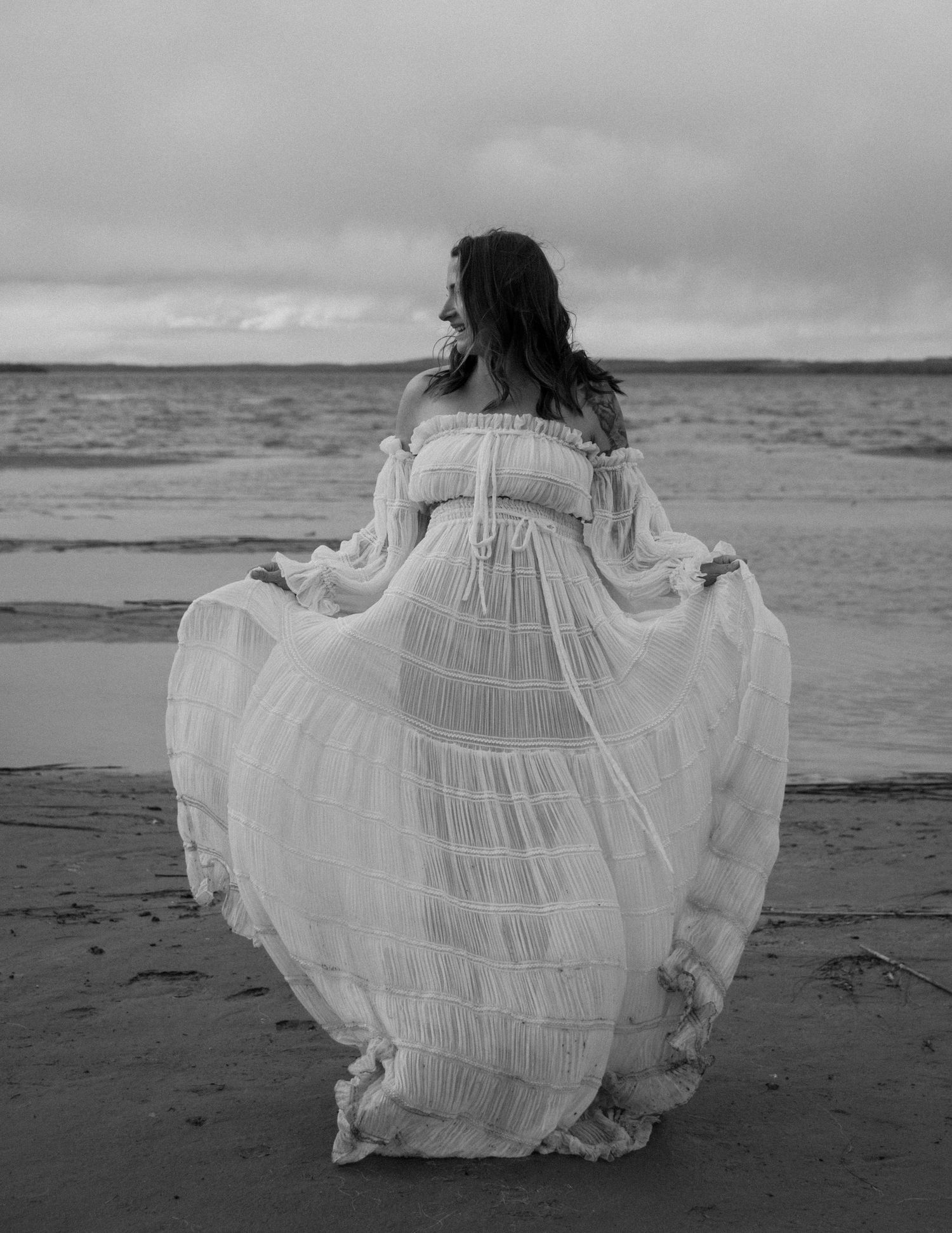 Dramatic black and white photo of flowing white dress on empty beach. Calgary Alberta Maternity Photographer.