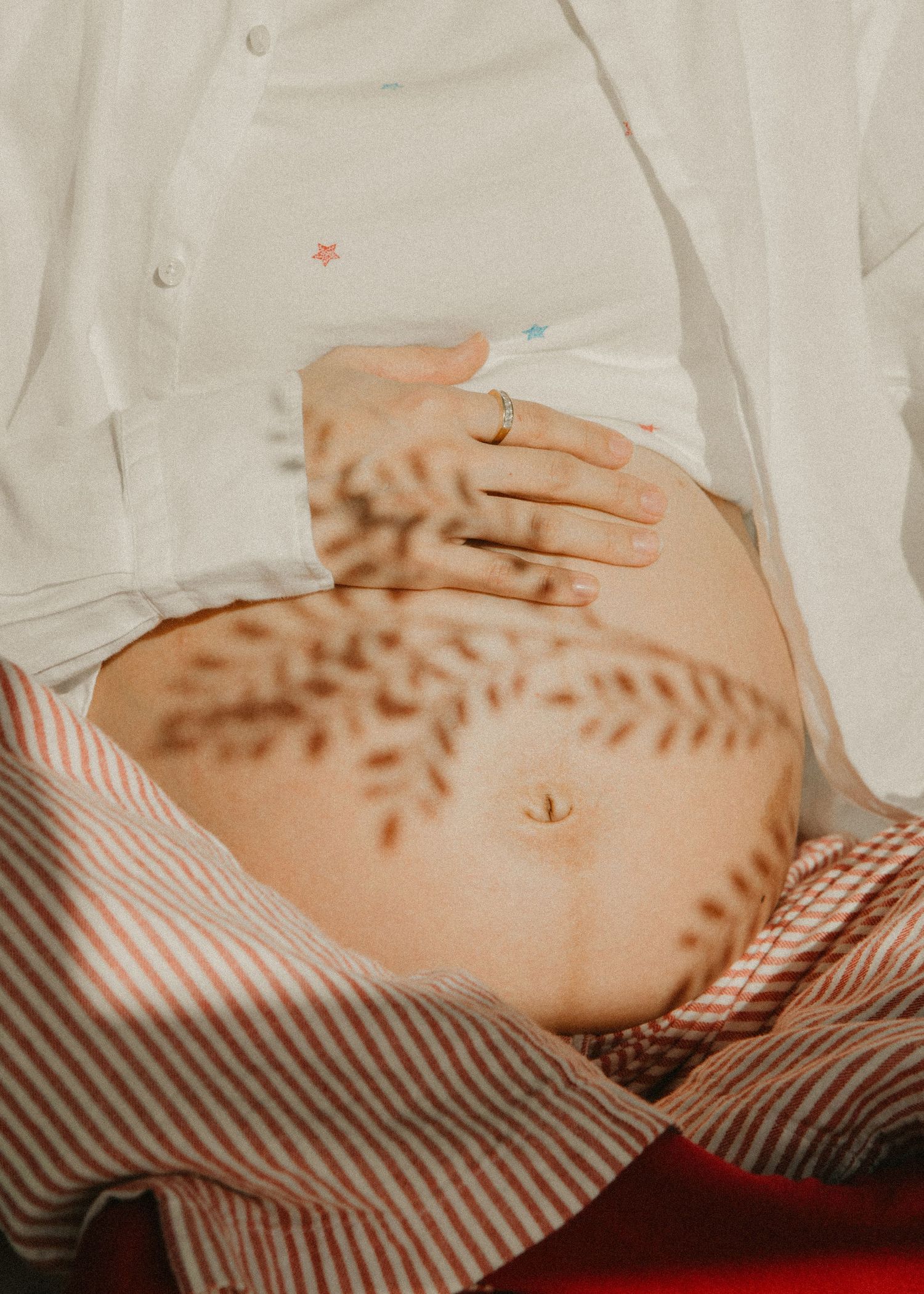 Artistic maternity photo showing sun-dappled shadows across pregnant belly. Calgary Alberta Maternity Photographer.