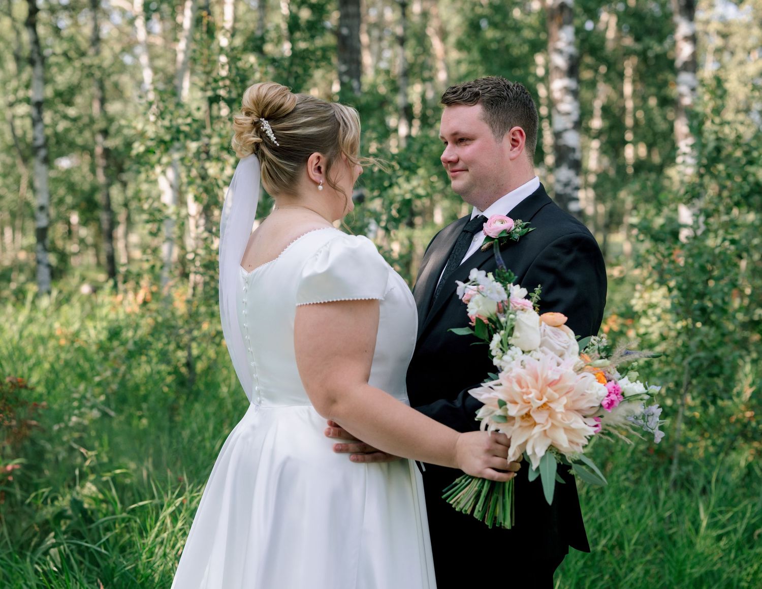 A bride and groom share intimate moments in a lush woodland setting during their wedding photoshoot.