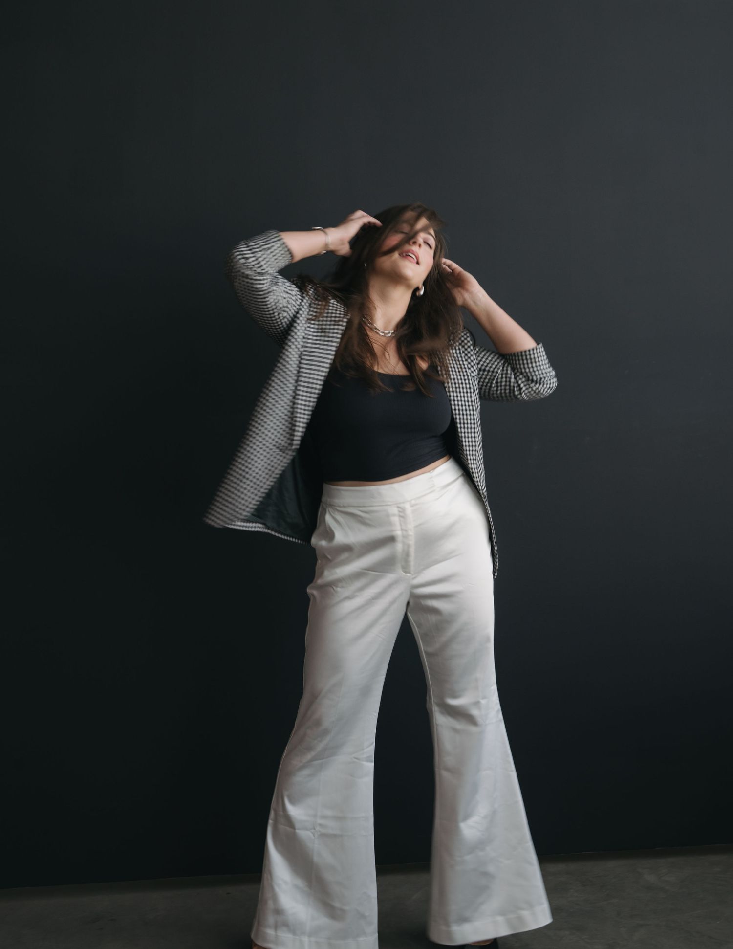 A person in a gray blazer and white flared pants strikes a dynamic pose against a dark background.