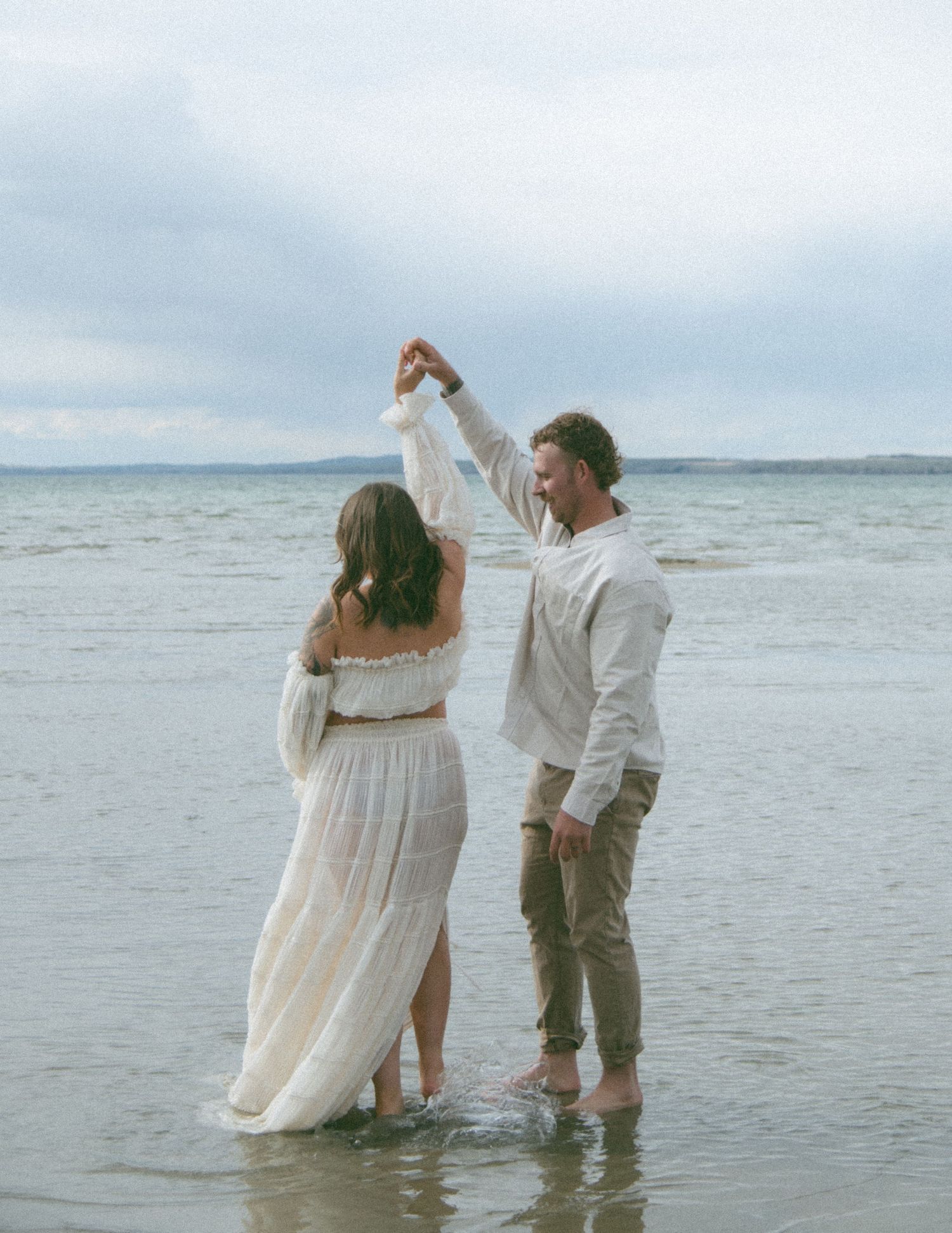 Joyful dance pose during a seaside maternity photoshoot. Calgary Alberta Maternity Photographer.