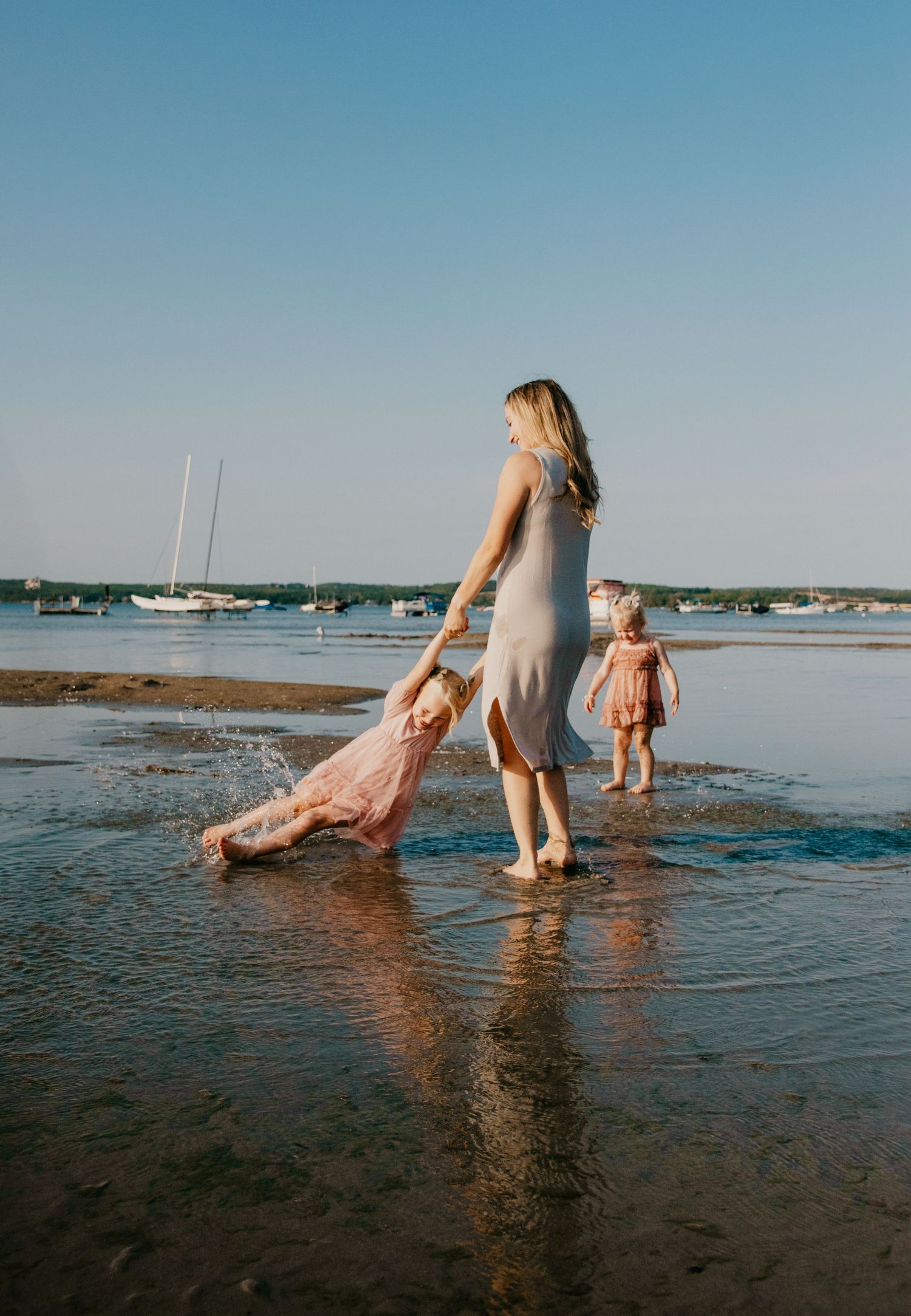 Parent and children playing in shallow coastal waters with boats in background. Calgary Family and Maternity Photographer