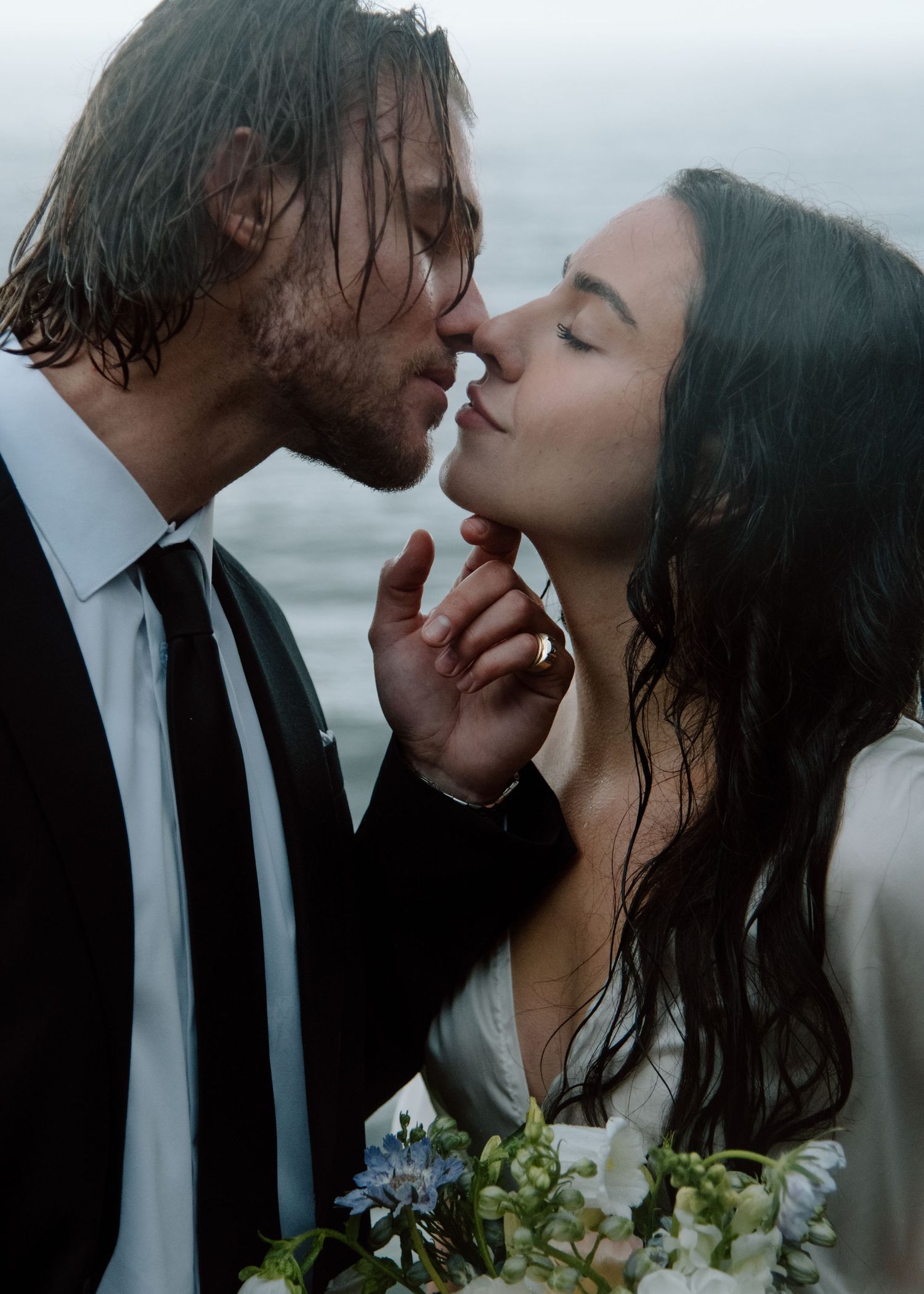 An intimate moment between newlyweds with rain-dampened hair against a misty coastal backdrop. Calgary Wedding Photographer