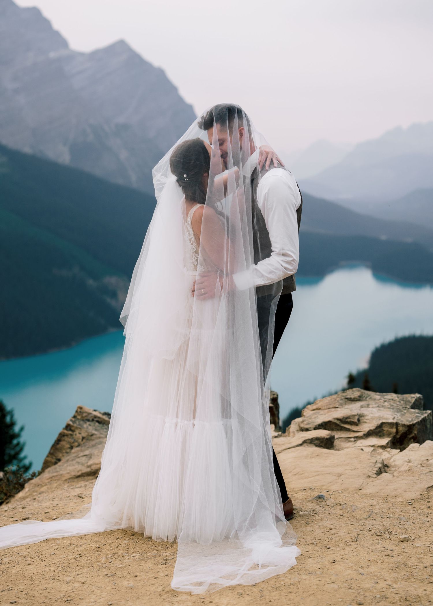 A romantic wedding couple shares an intimate moment at Lake Peyto viewpoint in Banff National Park, surrounded by mountains.
