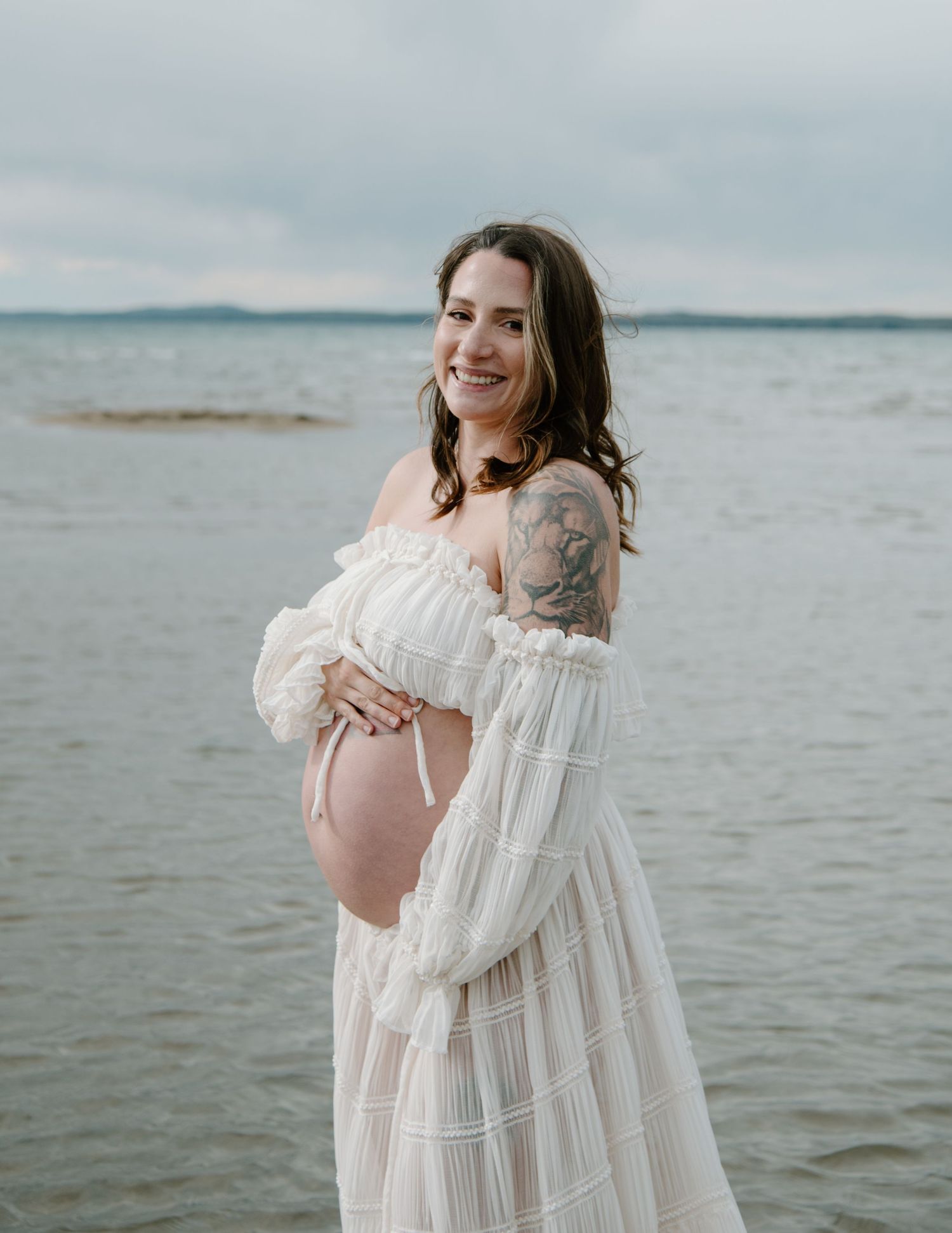 Flowy white off-shoulder dress twirling by the ocean's edge in soft light. Calgary Alberta Maternity Photographer.