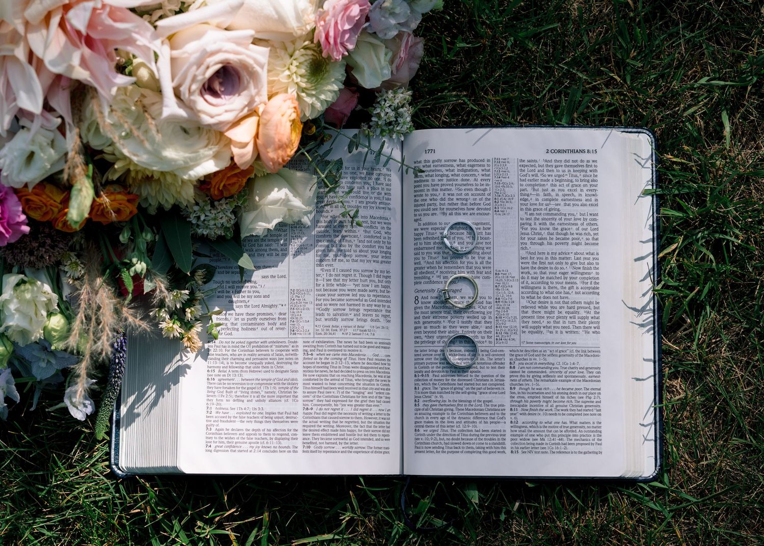 An open book lies on grass surrounded by delicate pink and white floral arrangements and decorative elements.