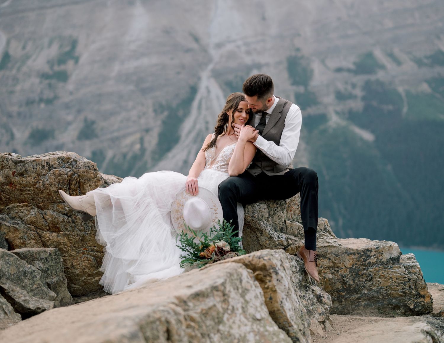 Newlyweds share romantic moments against dramatic mountain backdrop in Lake Louise during a destination wedding photoshoot.