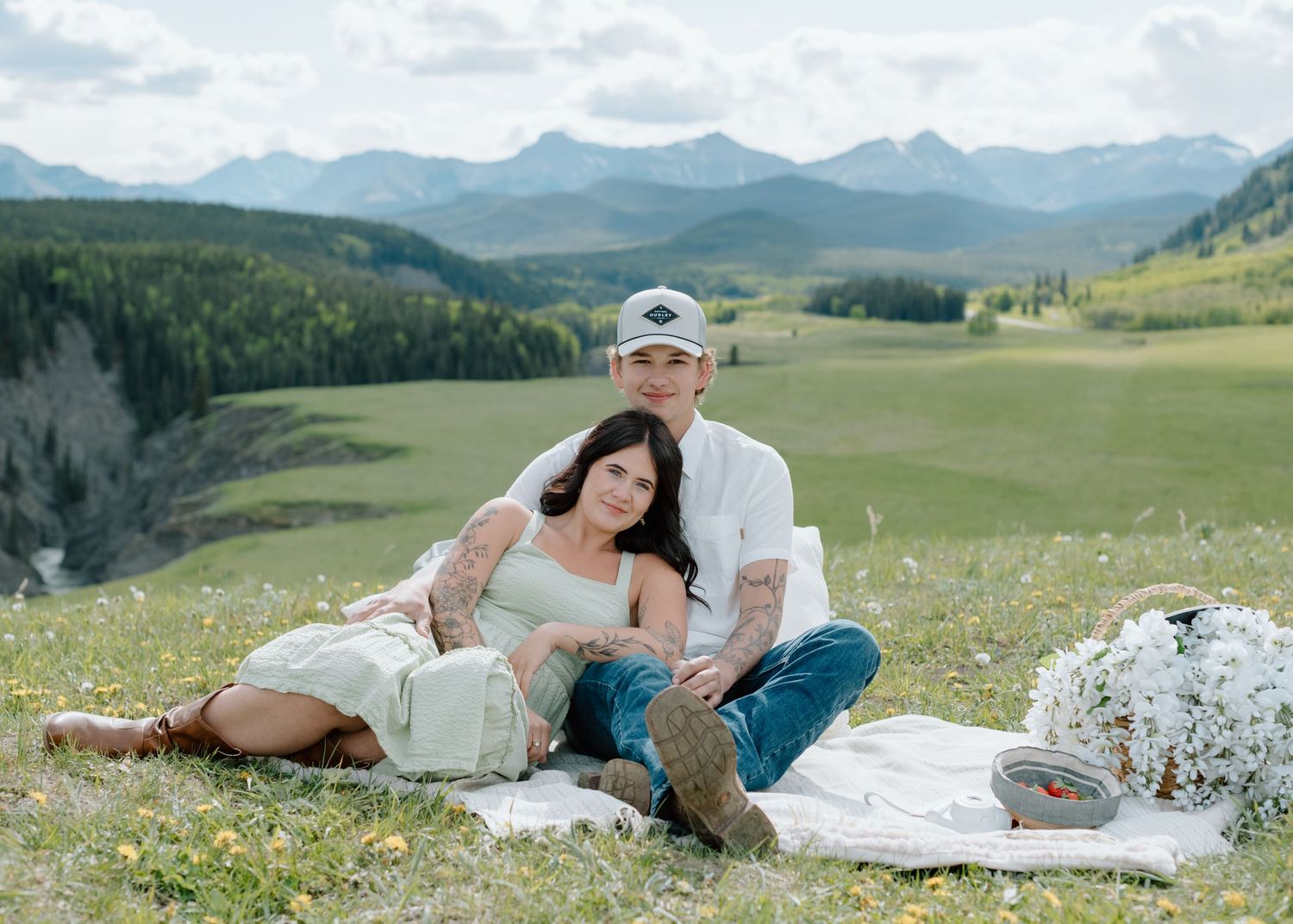 Relaxing on white blankets in a wildflower meadow with mountain ranges in the distance in Calgary, Alberta Calgary Lifestyle and Engagement