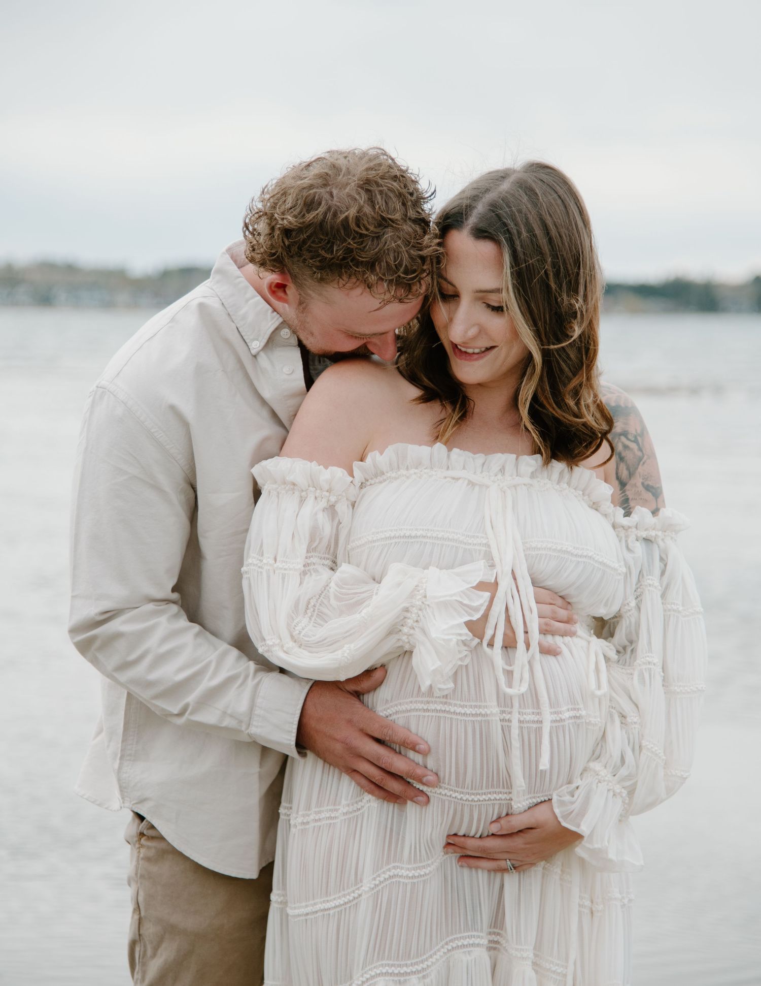 Serene beachfront maternity portraits featuring a couple in flowing white clothing. Calgary Alberta Maternity Photographer.