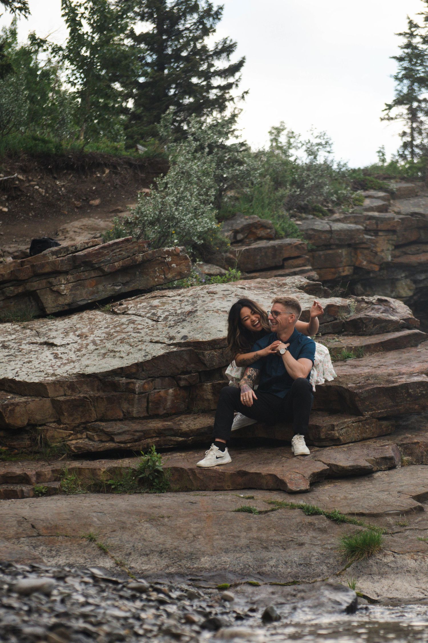 Couple lying together on rocky terrain near flowing water in Calgary Alberta. Calgary Lifestyle and Engagement Photographer.