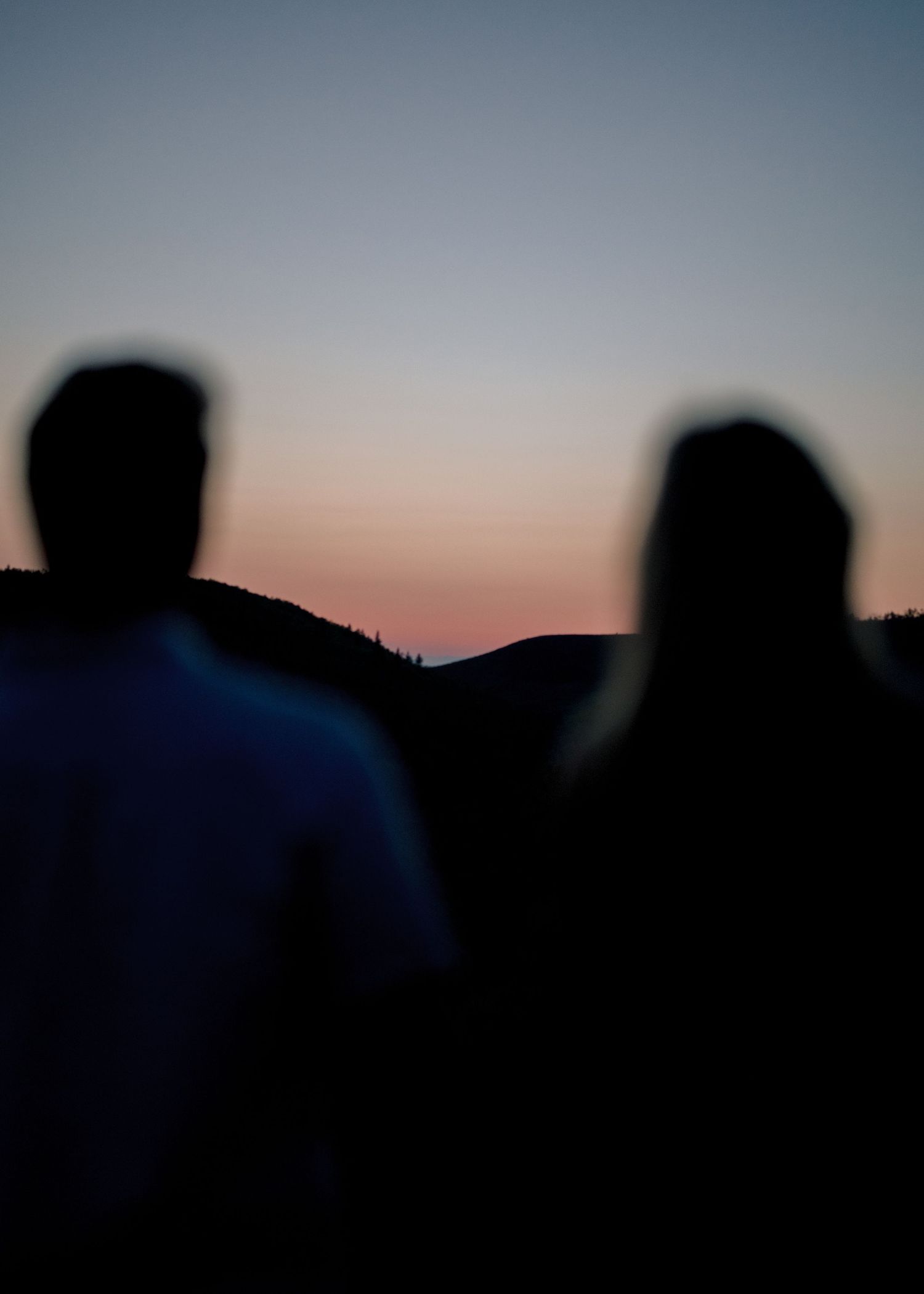 Silhouetted figures walking along a ridgeline against a colorful sunset sky, creating a dramatic mountain landscape view.