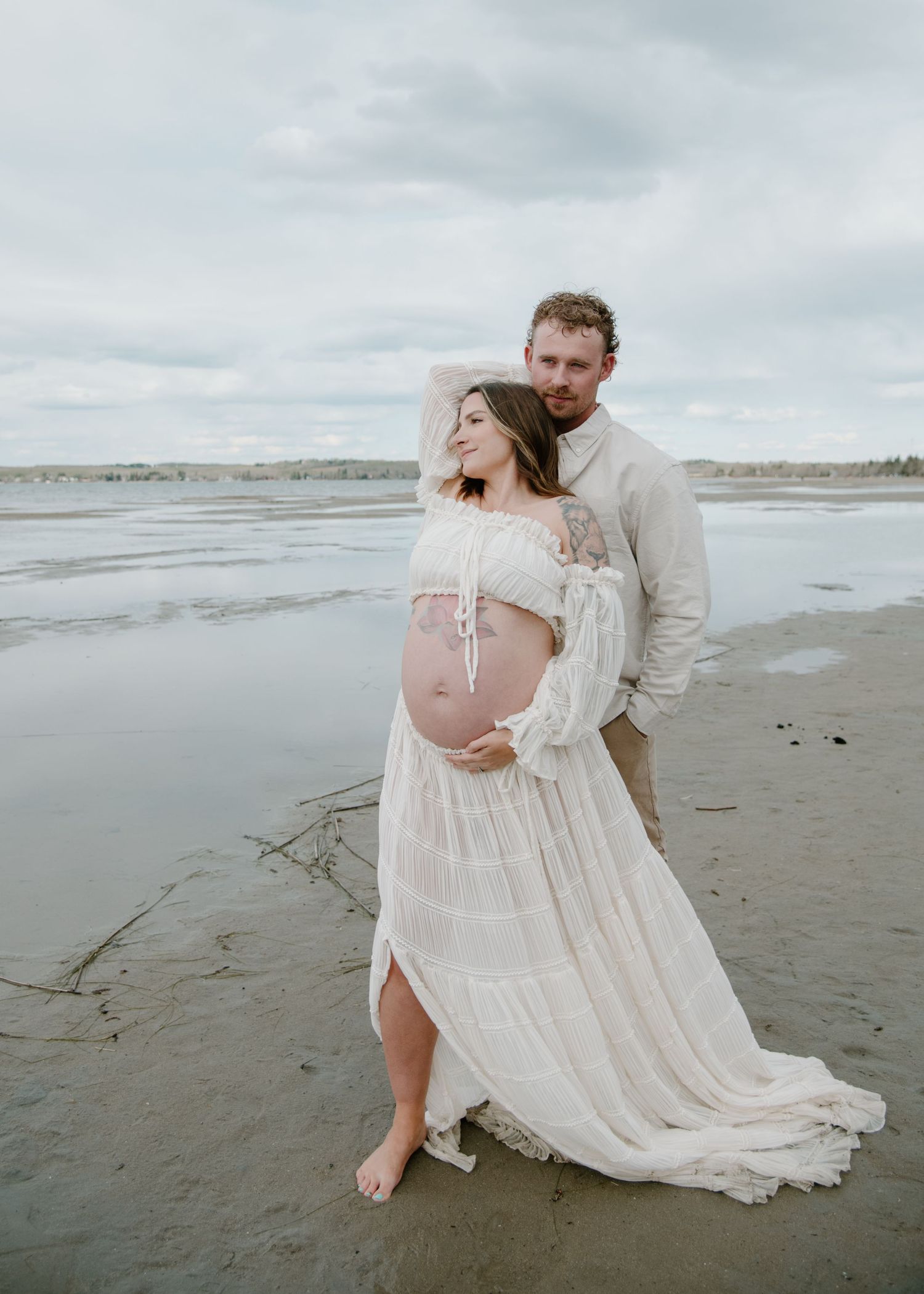 Artistic maternity beach photos with flowing white dress against moody sky. Calgary Alberta Maternity Photographer.