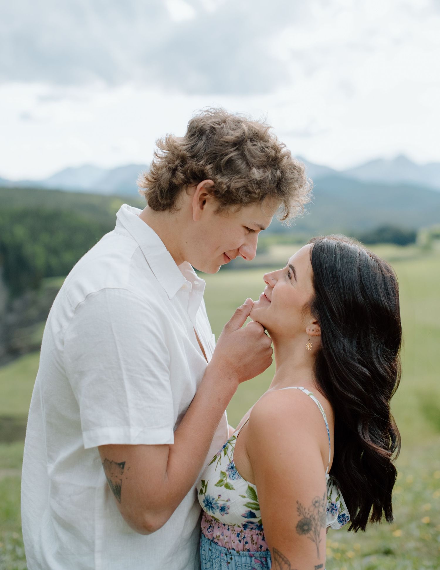 A tender moment between two people in a mountain field with dramatic cloudy skies. Calgary Alberta Engagement Photographer.