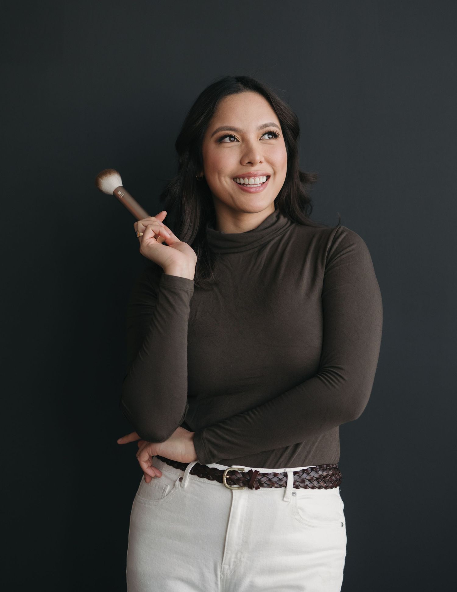 A person in a brown turtleneck and white pants poses against a dark background in a series of casual expressions.