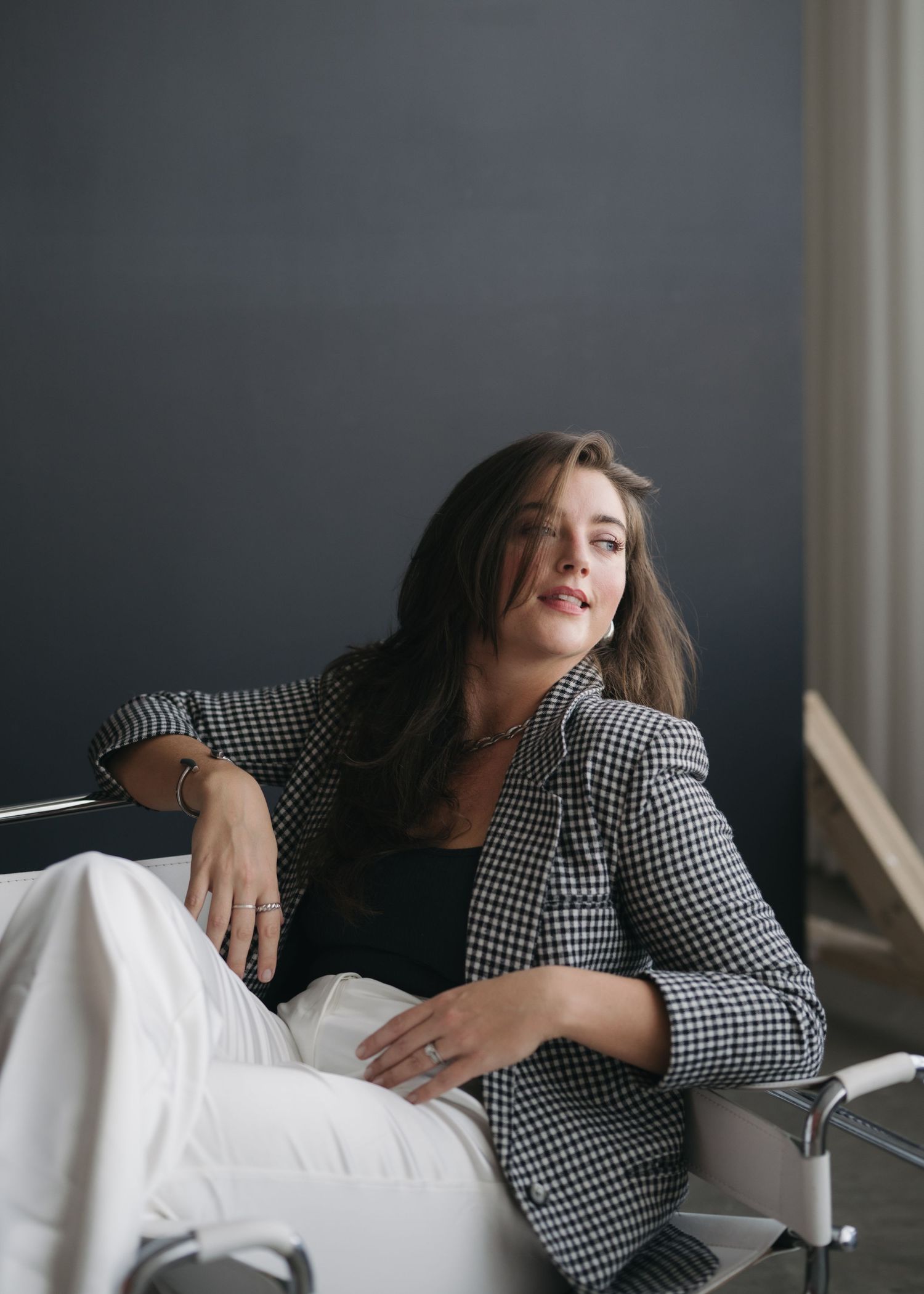 A person in a black and white checkered blazer reclines on a white couch in dramatic lighting.
