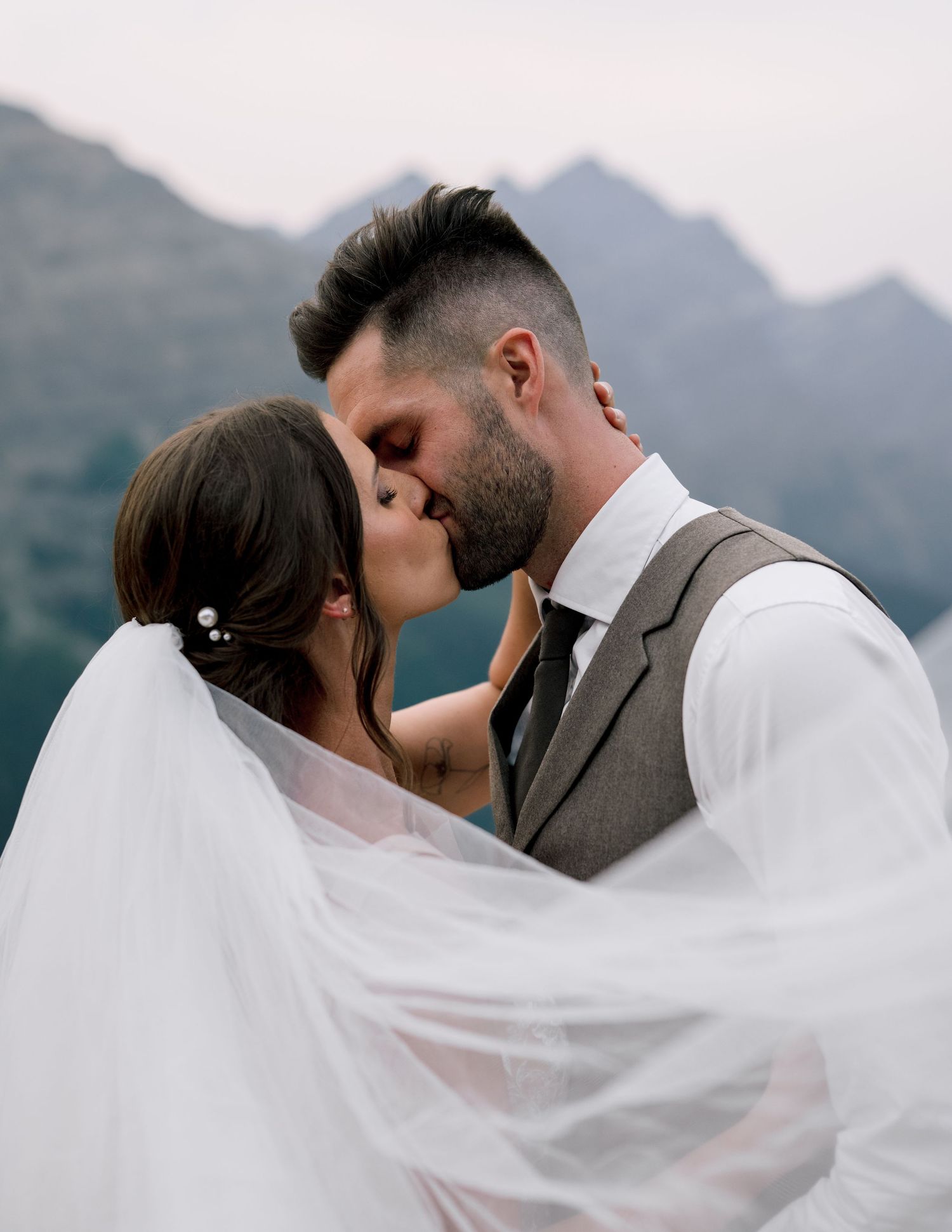Romantic veil shot sequence of newlyweds kissing with mountain backdrop during golden hour.